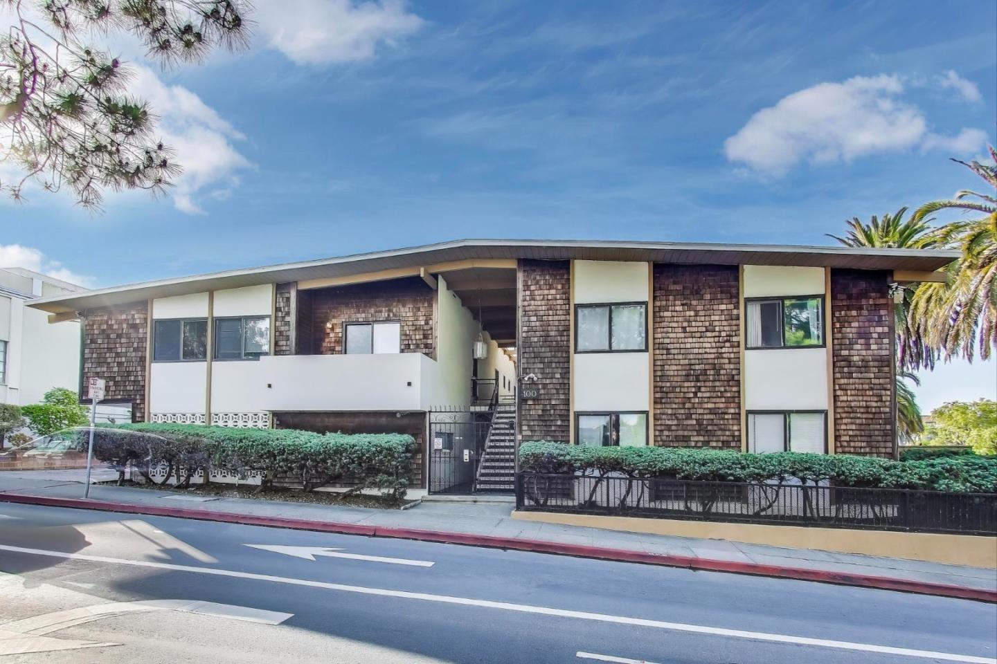 Two-story residential building with shingle siding, central gated entrance, and palm trees.