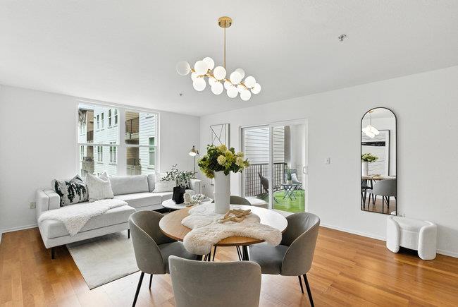 Staged living and dining room with hardwood floors, round table, gray sofa, and balcony access.