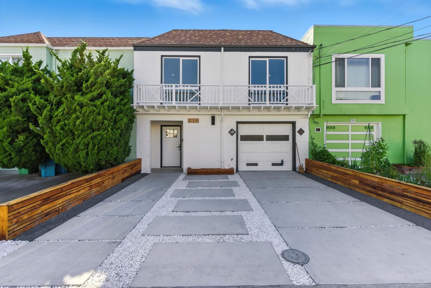 White two-story home with a balcony and broad concrete-and-gravel driveway.