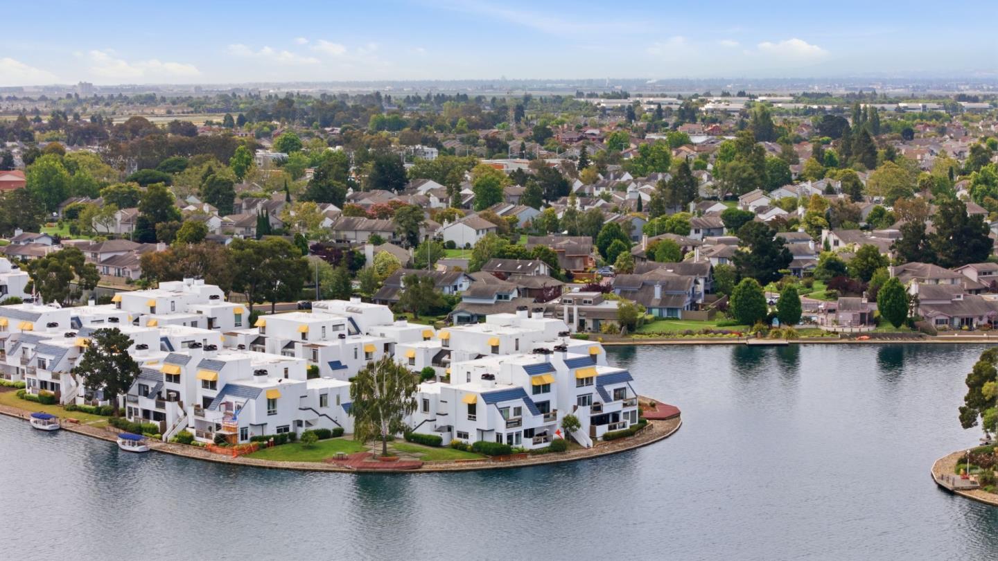 Aerial view of white waterfront homes beside a lagoon, with a leafy residential neighborhood beyond.