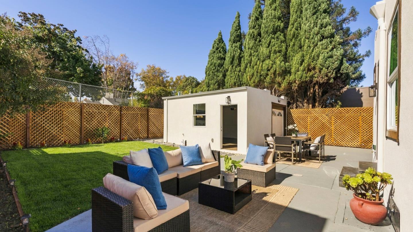 Backyard patio with wicker lounge seating, dining area, lawn, and detached outbuilding.