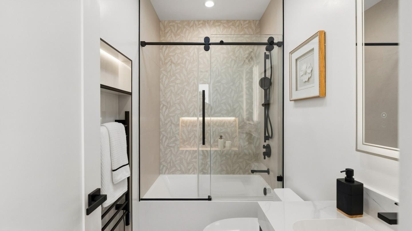 Bathroom with a glass-enclosed tub and shower, patterned tile, and matte black fixtures.