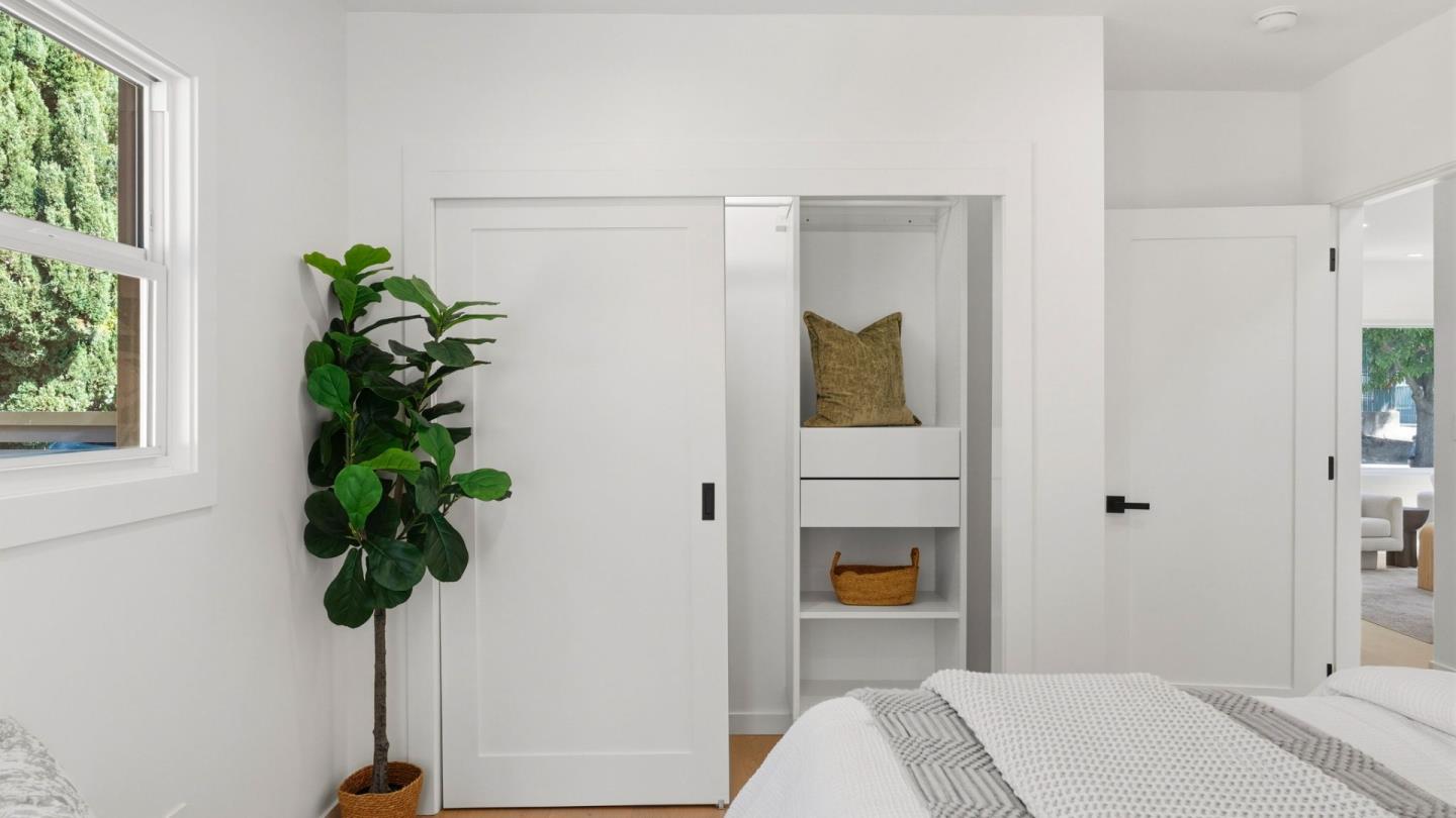 Bright bedroom with white bedding, an open built-in closet, and a leafy plant beside the window.