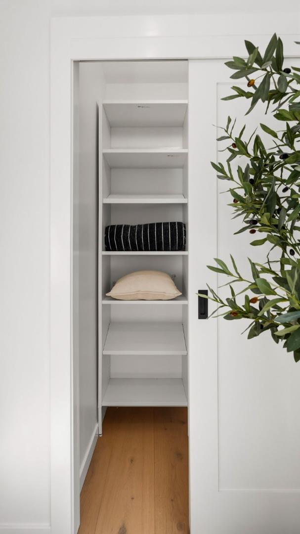 Walk-in closet with built-in white shelves, cushions, and warm wood flooring.