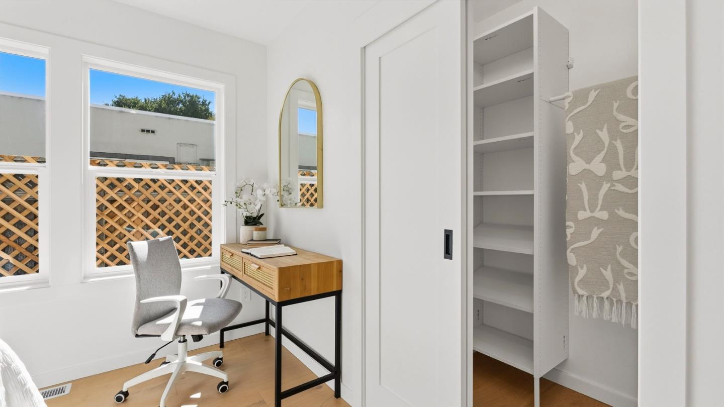 Bright home office with a wooden desk, gray chair, sunny windows, and open closet shelves.