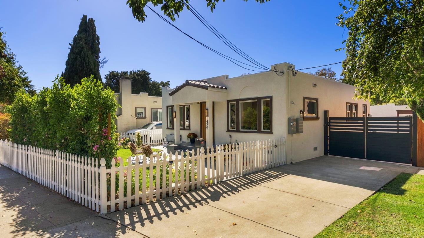 Single-story stucco home with a white picket fence, landscaped yard, and gated driveway.