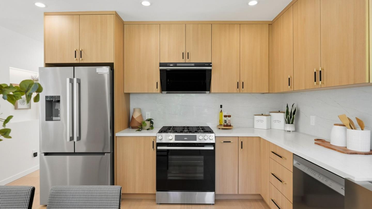 Kitchen with light wood cabinets, white counters, stainless refrigerator, and black range.