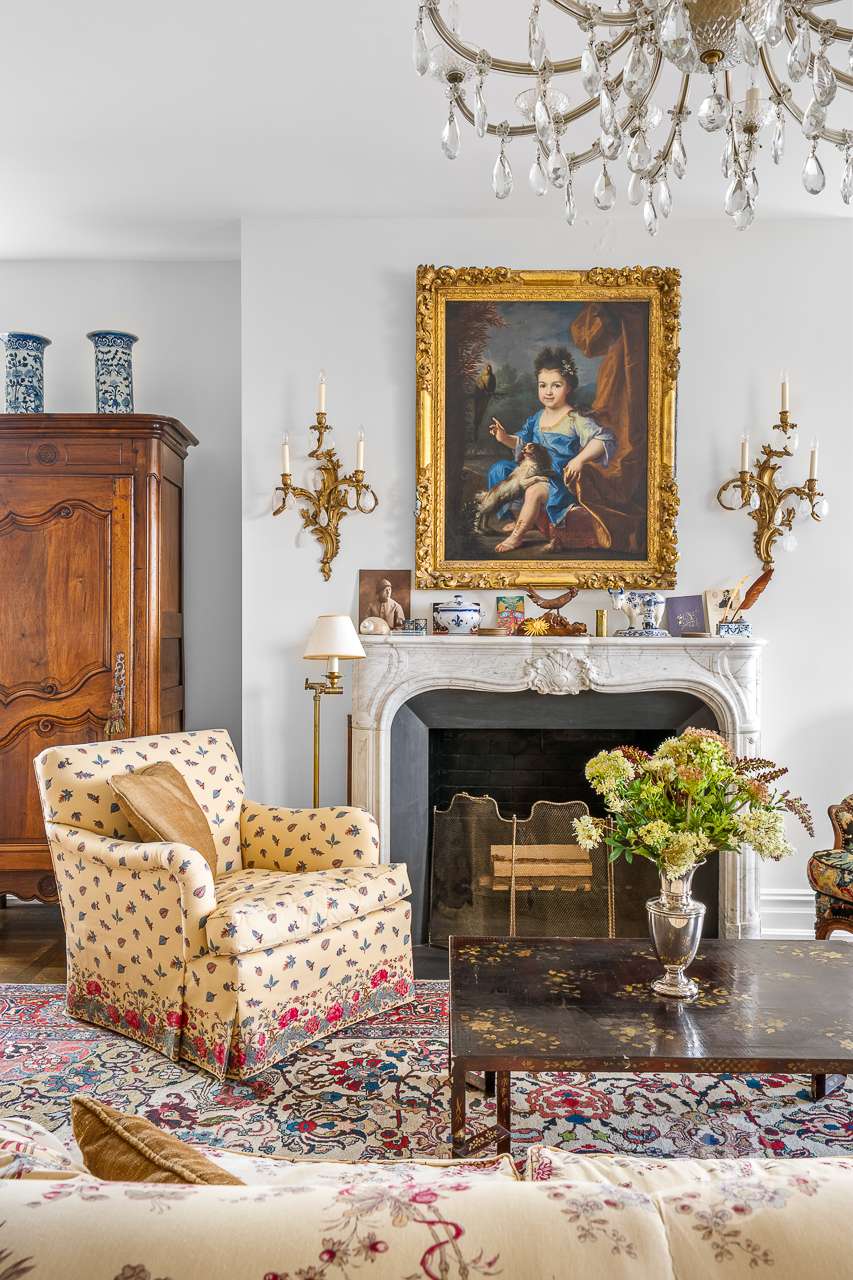 Living room with a marble fireplace, crystal chandelier, and gilded portrait above the mantel.