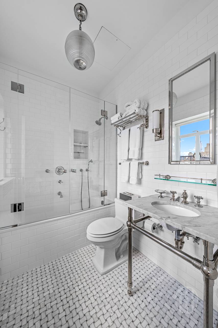 White bathroom with glass-enclosed tub, marble vanity, and patterned mosaic floor.