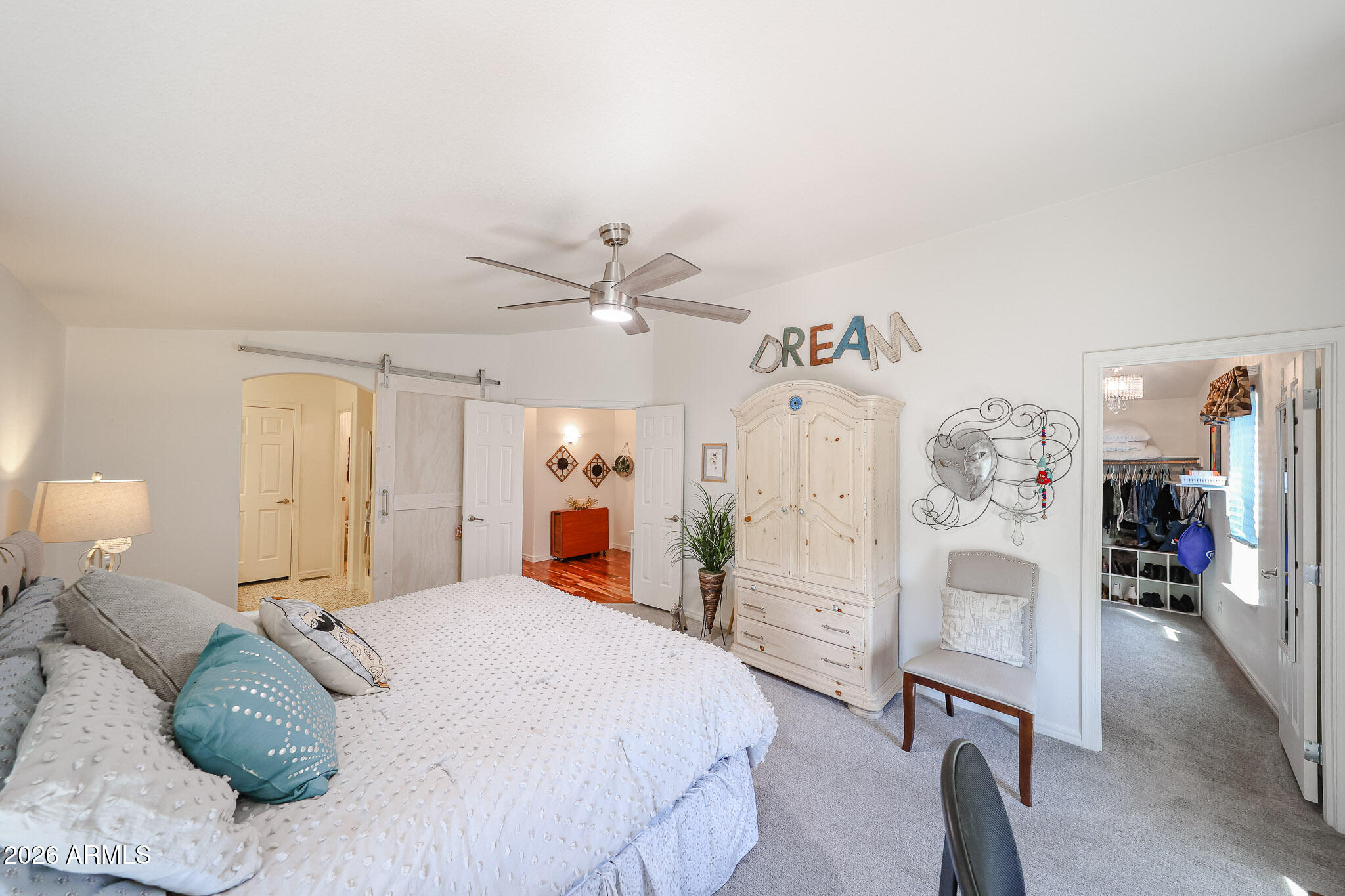 Furnished bedroom with a white bed, turquoise pillow, vintage-style armoire, and adjoining walk-in closet.