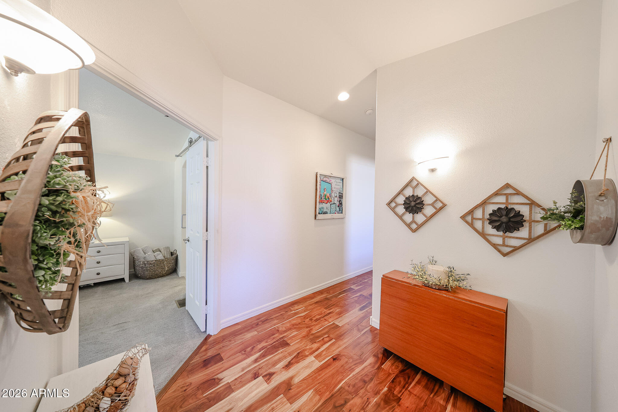 Entry hall with warm wood flooring, a reddish wood console, and a view into a carpeted room.