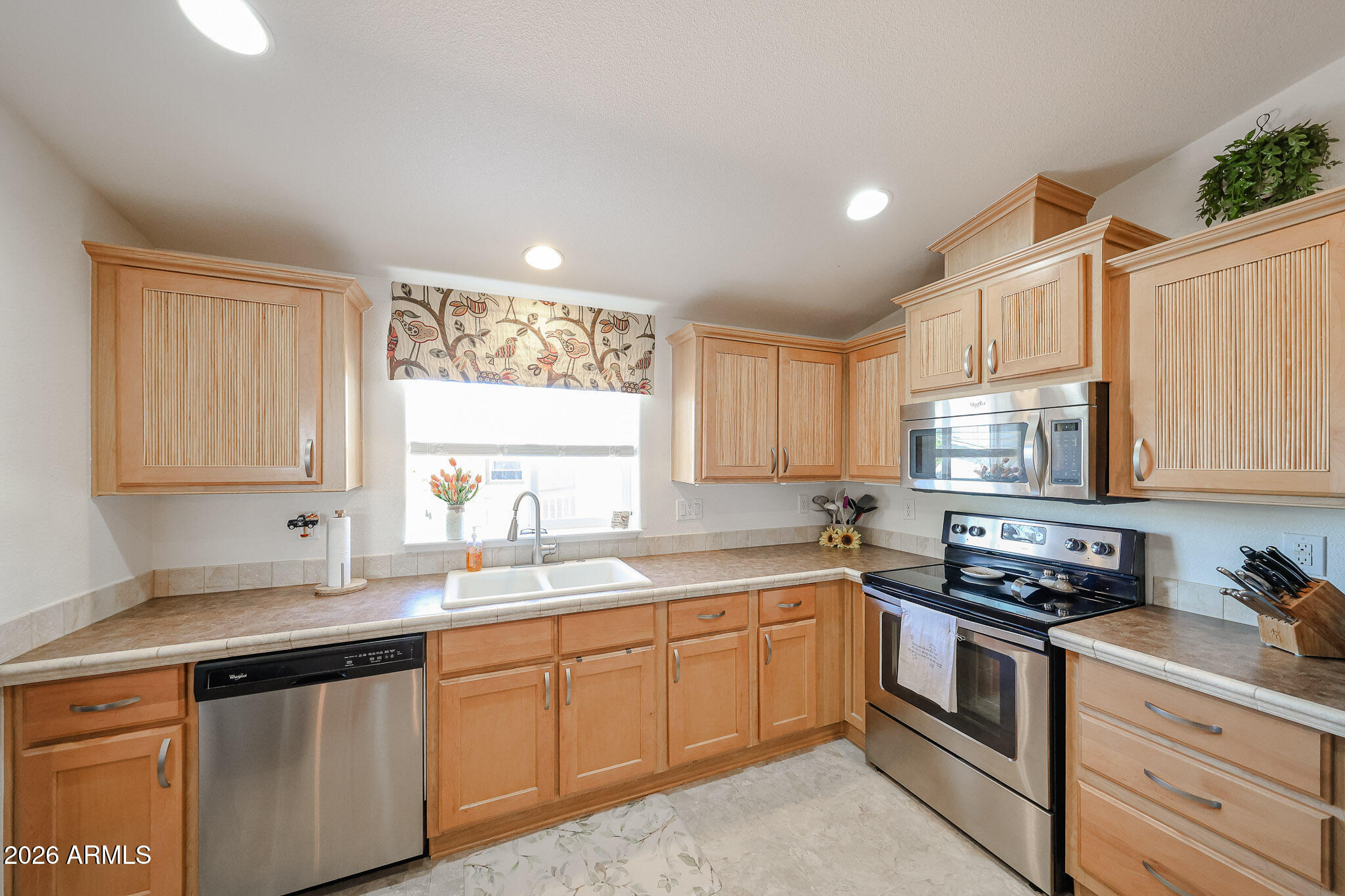 Kitchen with light wood cabinets, stainless steel appliances, and a double-basin sink beneath a window.