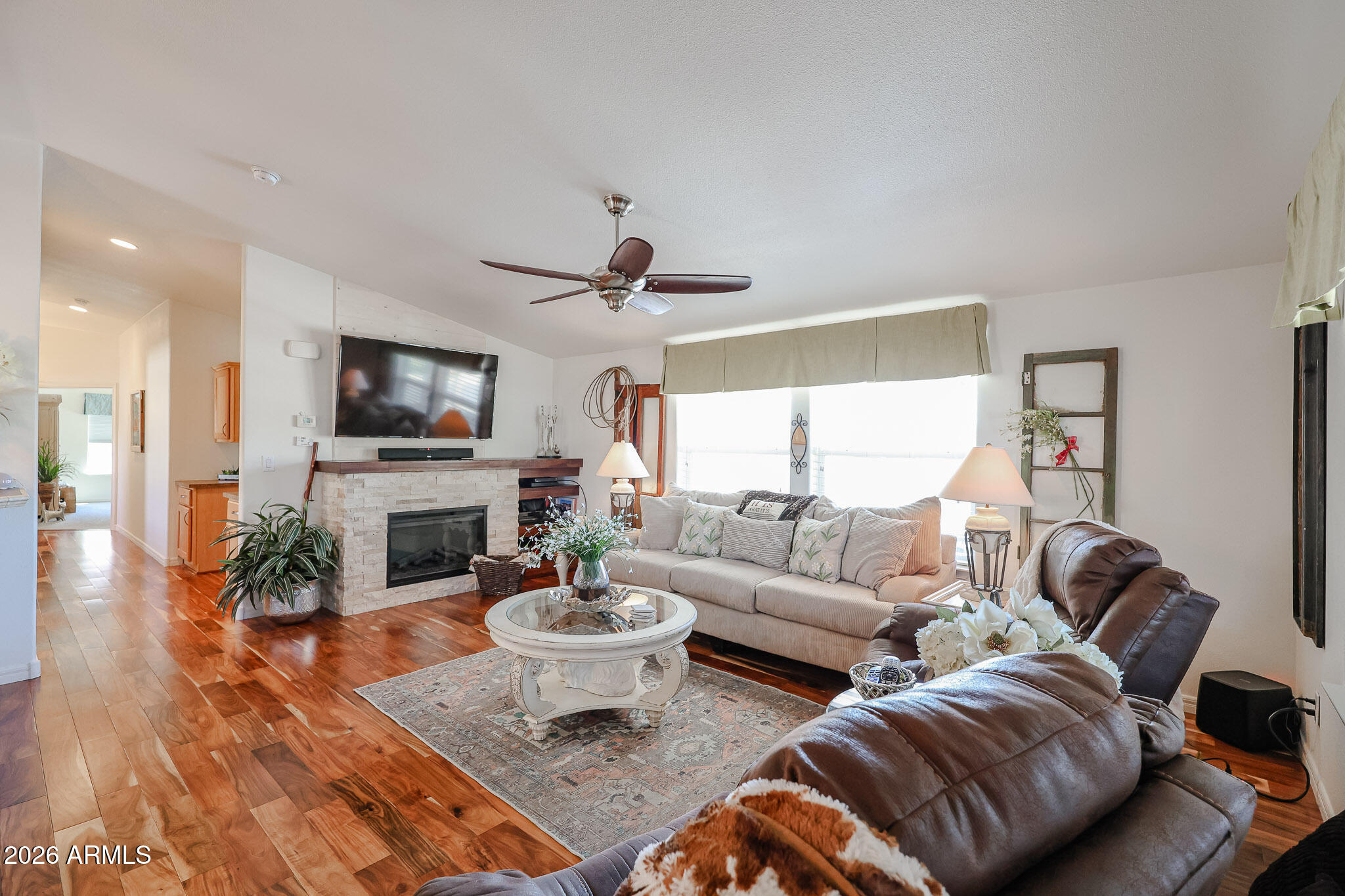 Living room with a stone fireplace, warm wood floors, beige sofa, and leather recliners.