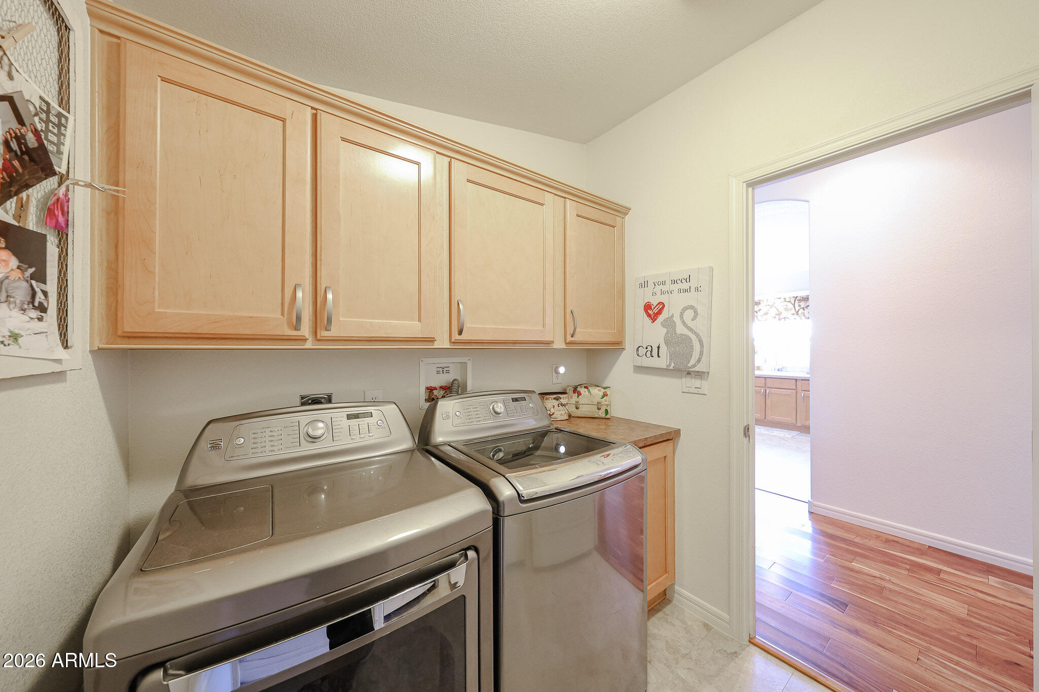 Laundry room with front-loading washer and dryer beneath light wood cabinets.