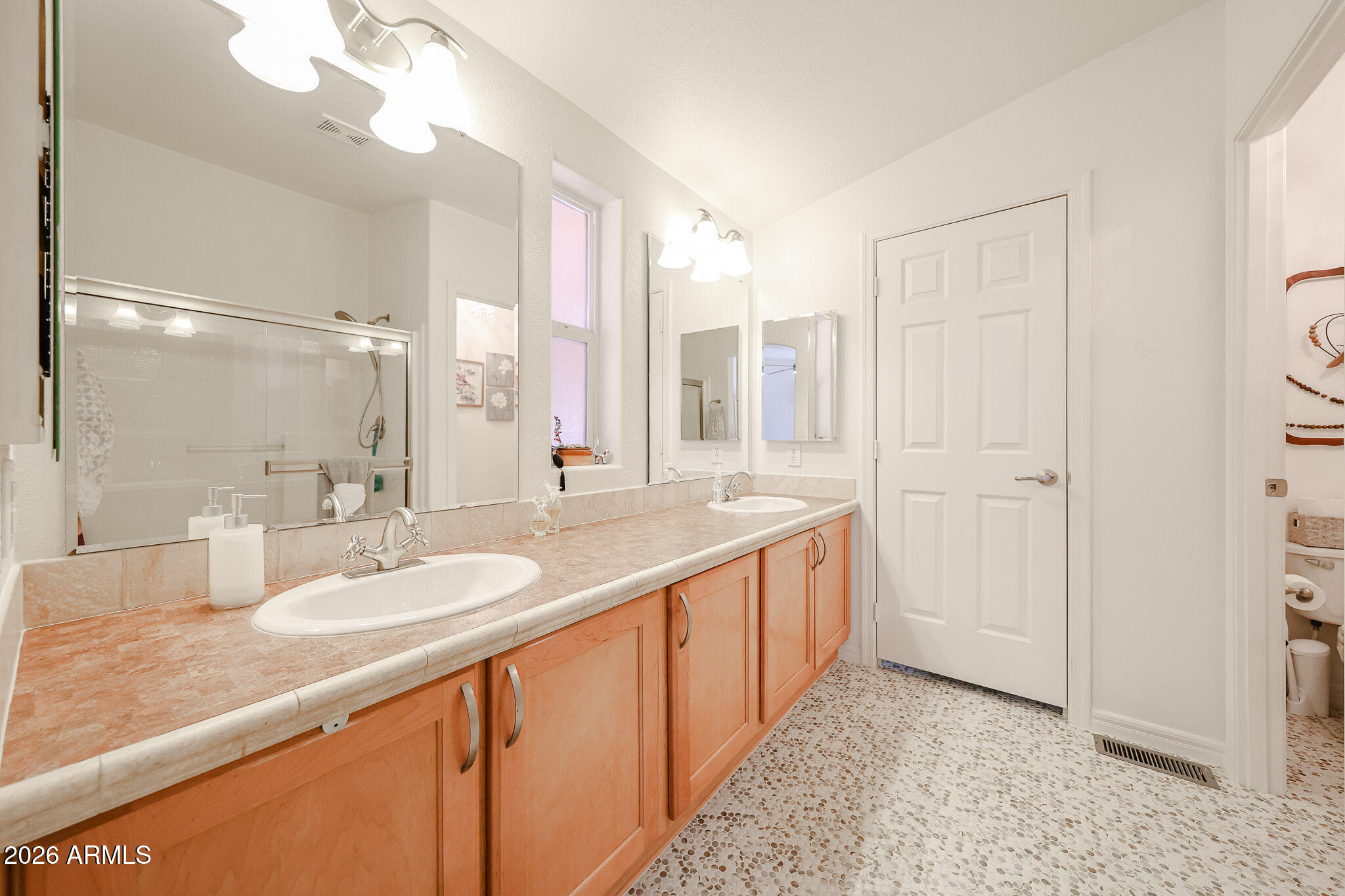 Bathroom with a double-sink vanity, large mirrors, glass shower, and pebble-patterned floor.