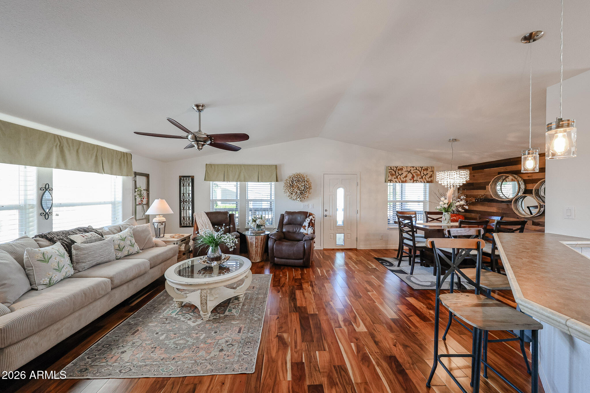 Open-plan living and dining room with polished wood floors and a wood-plank accent wall.