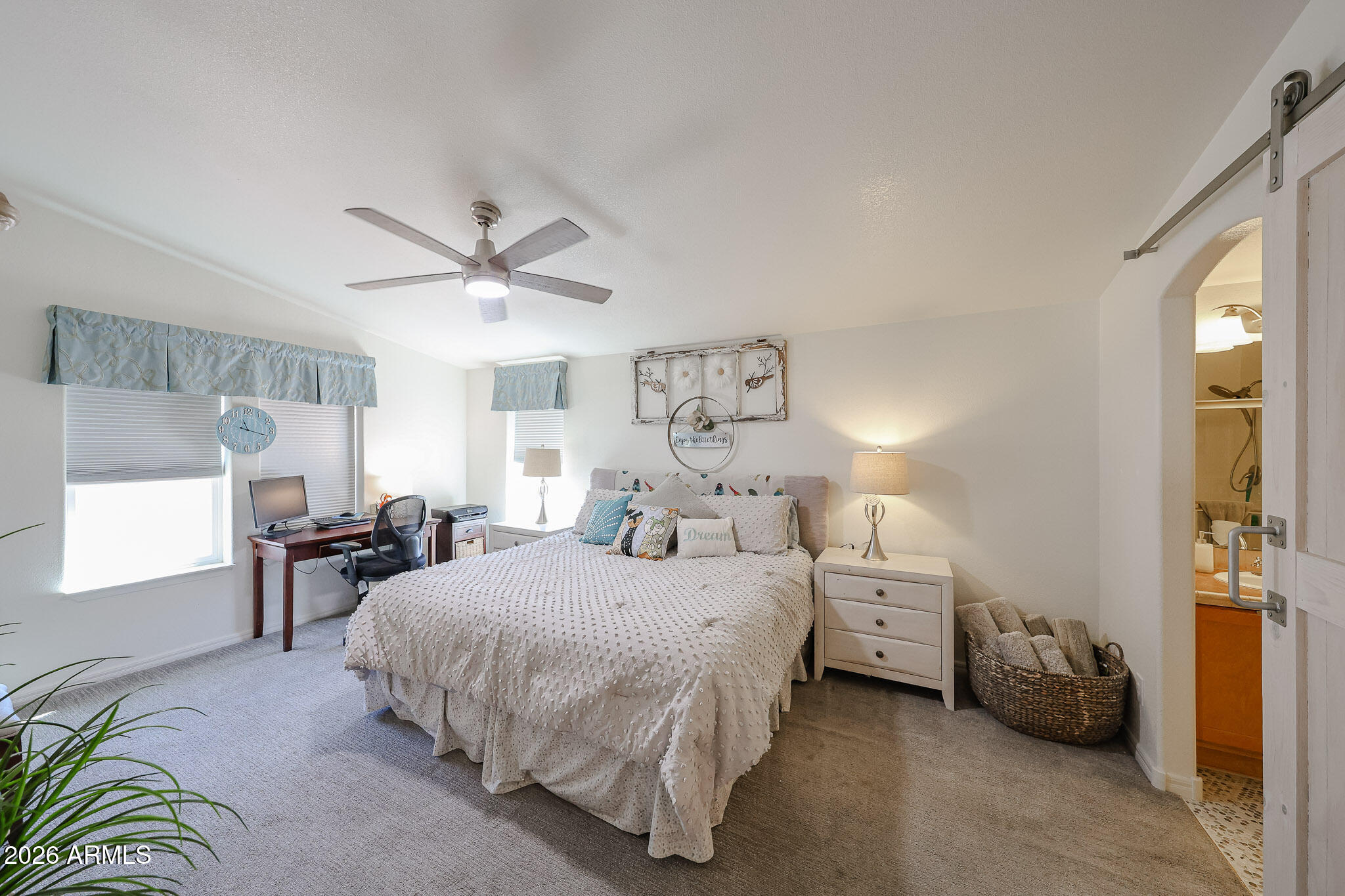 Furnished bedroom with a large white bed, desk by the windows, and an open sliding door to the bathroom.