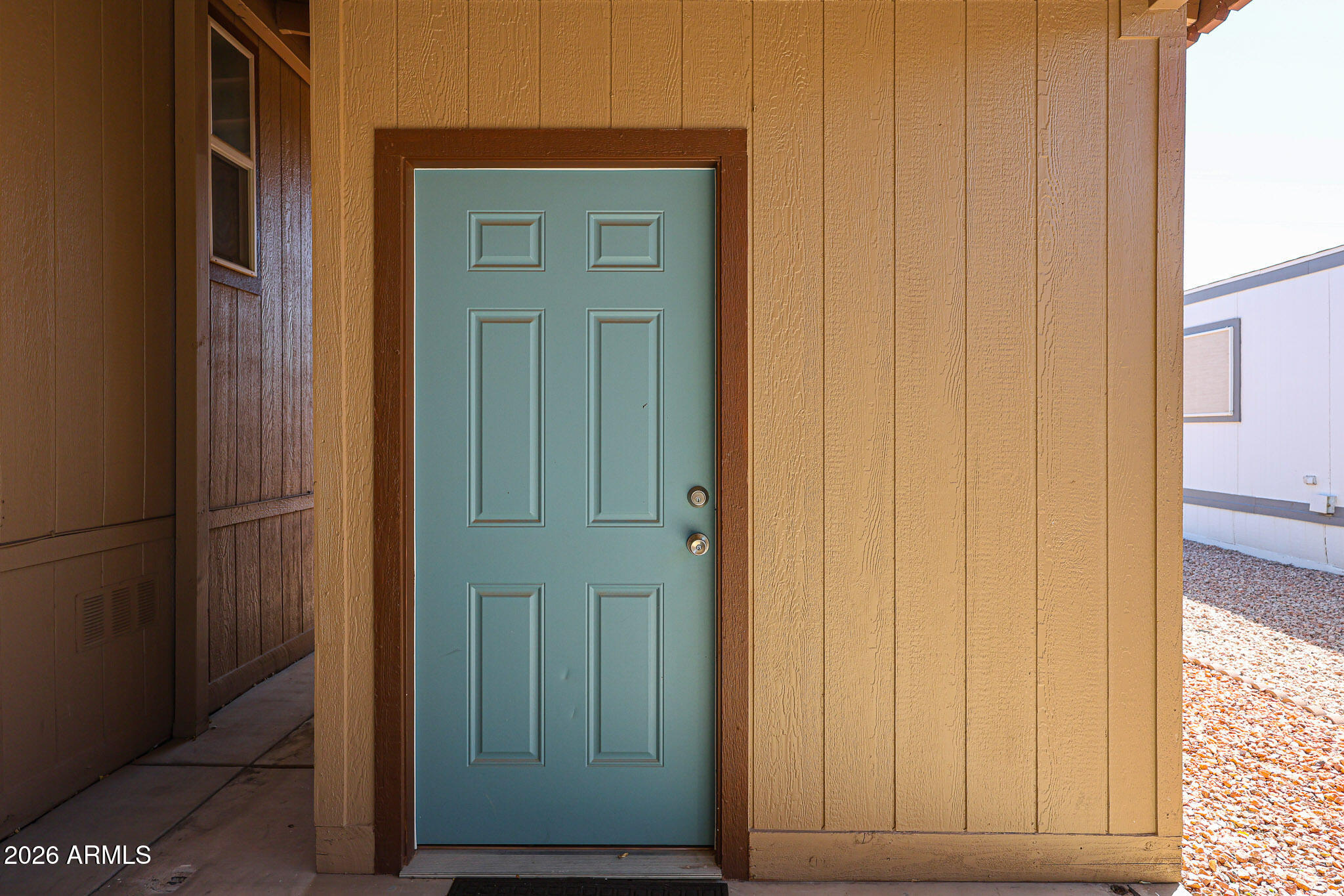 Blue-green paneled entry door with two locks, framed by tan siding and dark wood trim.