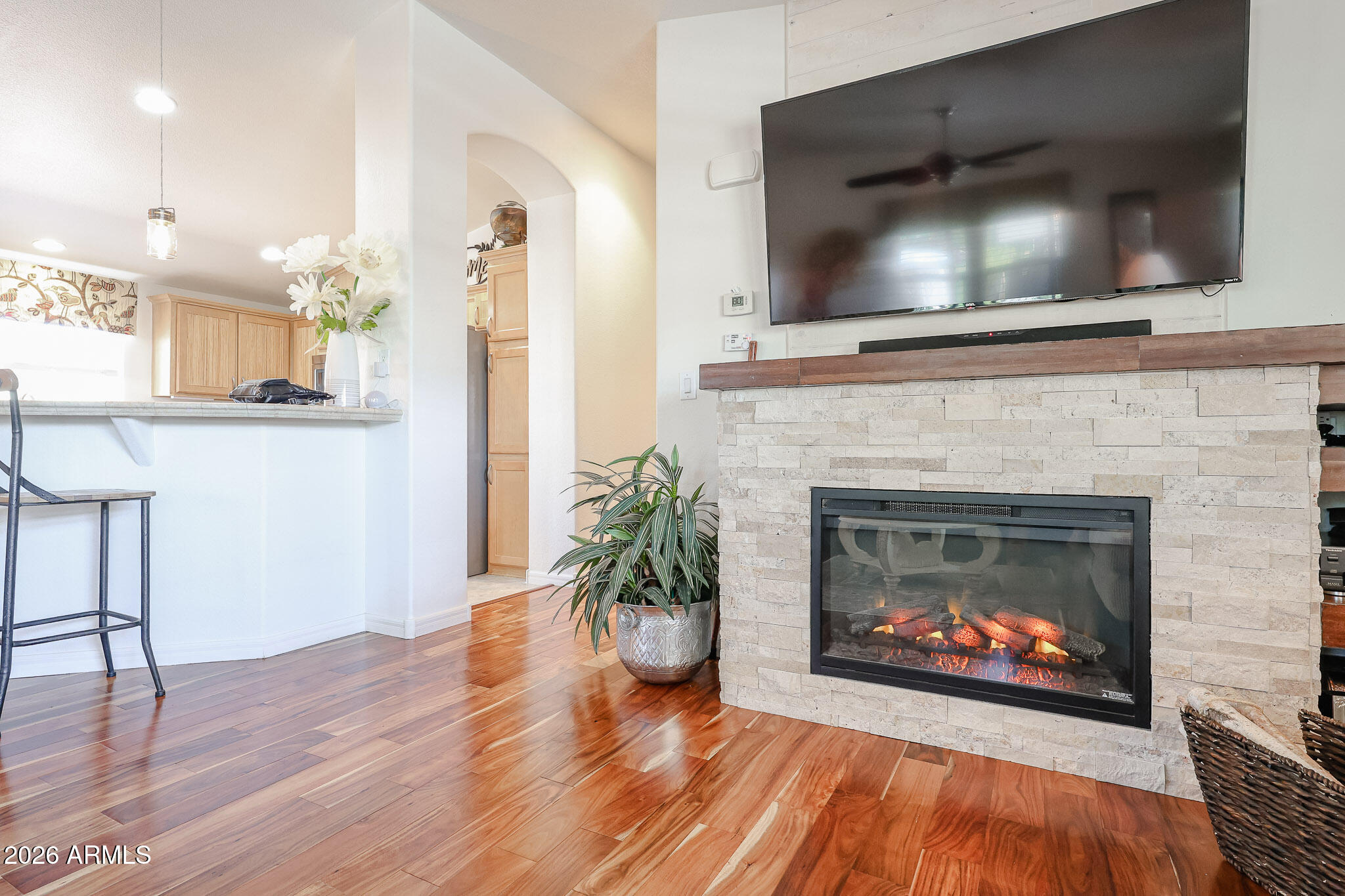 Living room with a stone fireplace, wall-mounted television, and glossy hardwood floors.