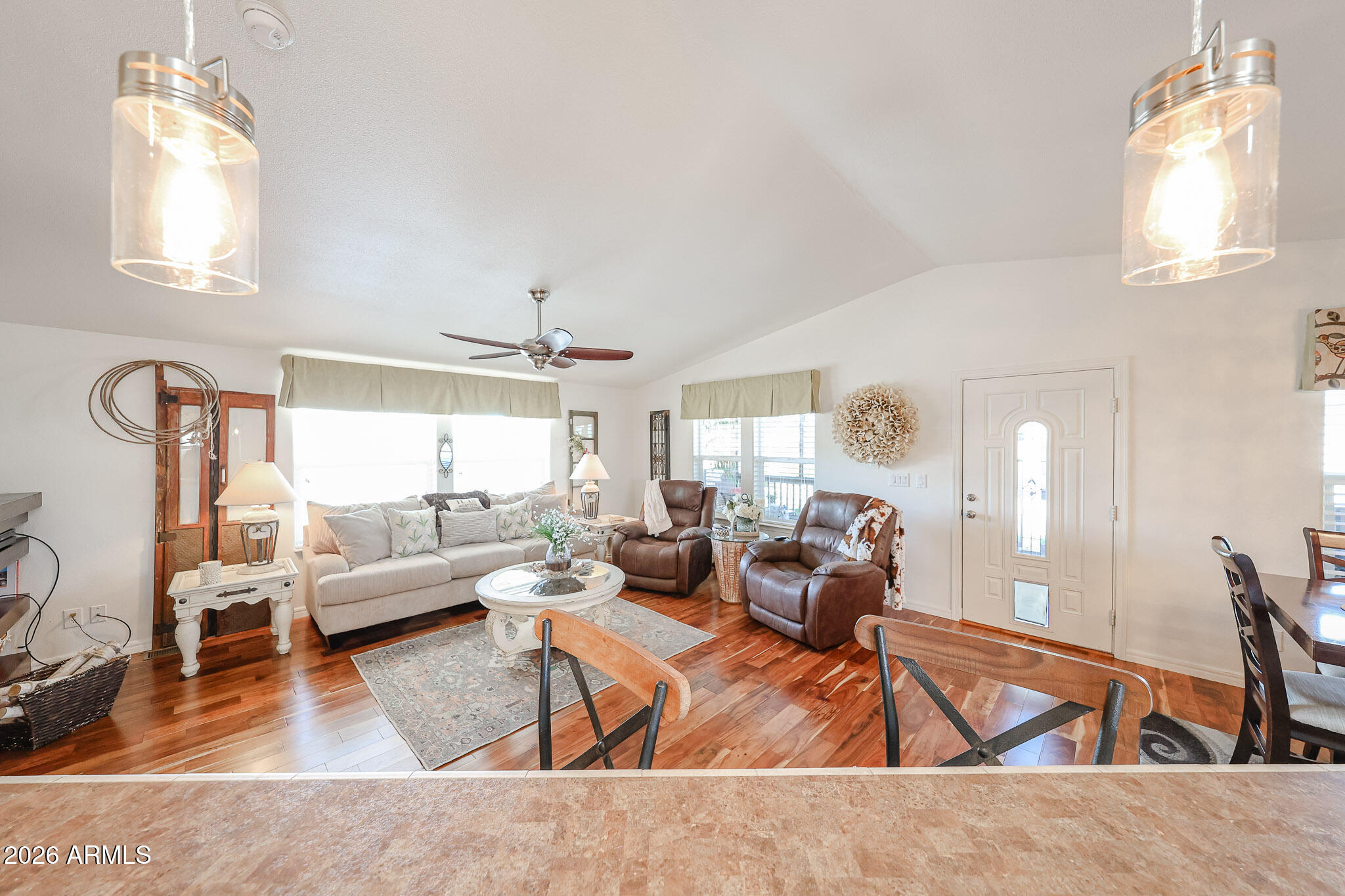 Furnished living room with a cream sofa, brown recliners, vaulted ceiling, and hardwood floors.