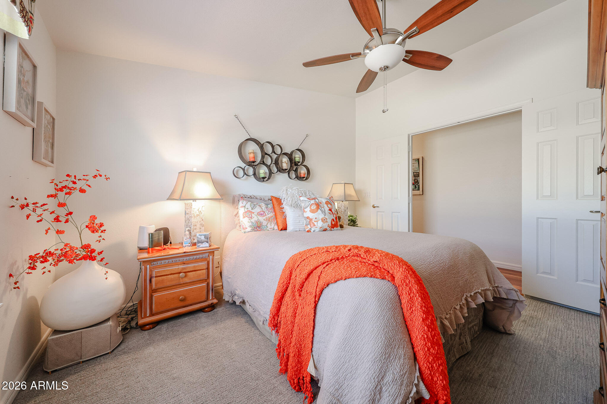 Furnished bedroom with a coral throw on the bed, matching bedside lamps, and a wood-blade ceiling fan.
