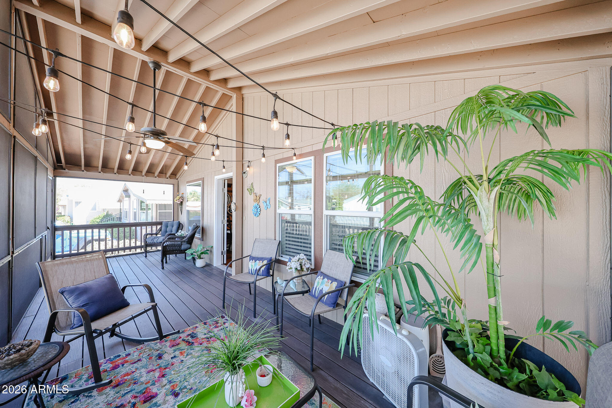 Covered patio with string lights, dark decking, seating, and large potted palms.