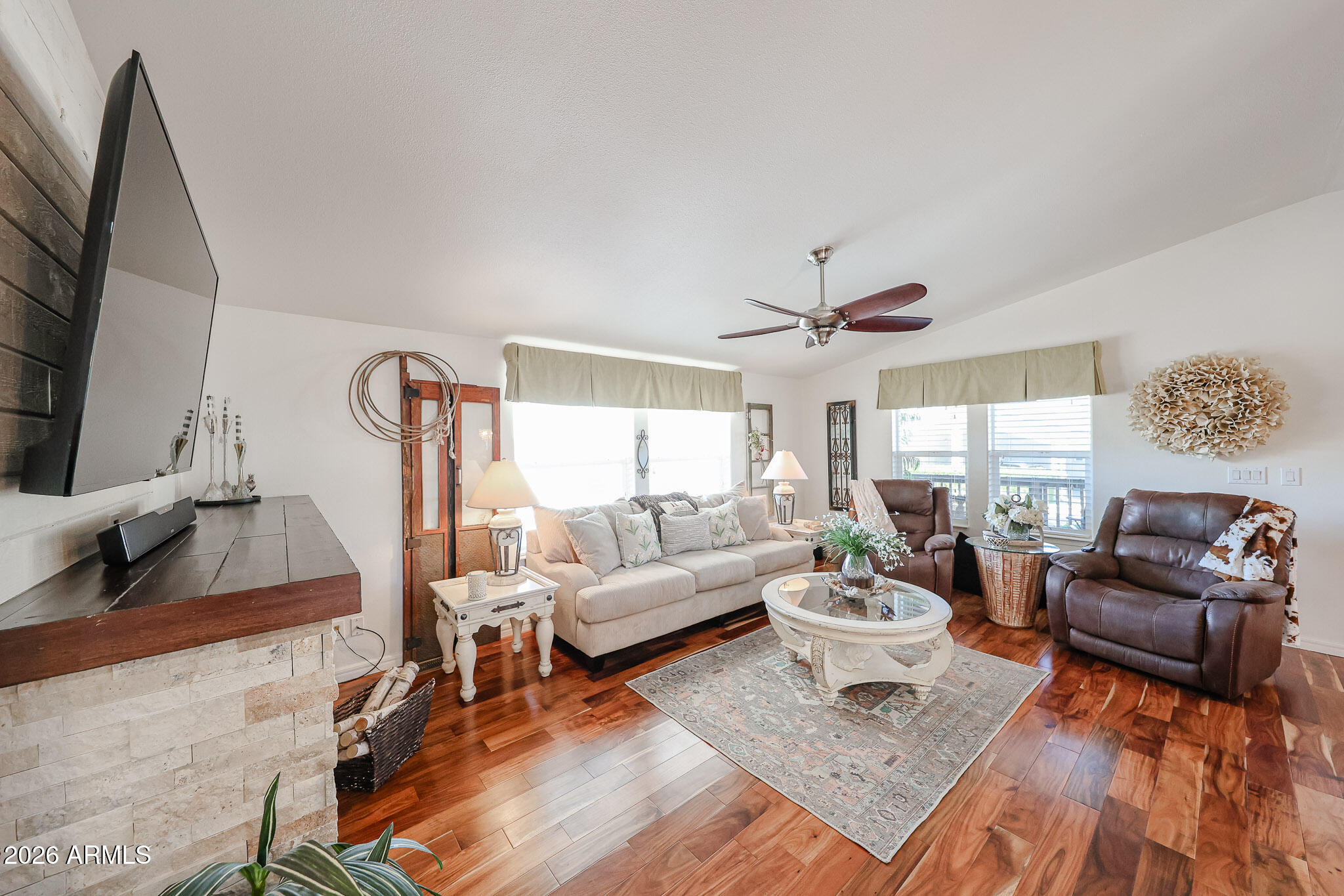 Living room with a cream sofa, leather recliners, stone fireplace, and polished wood floors.