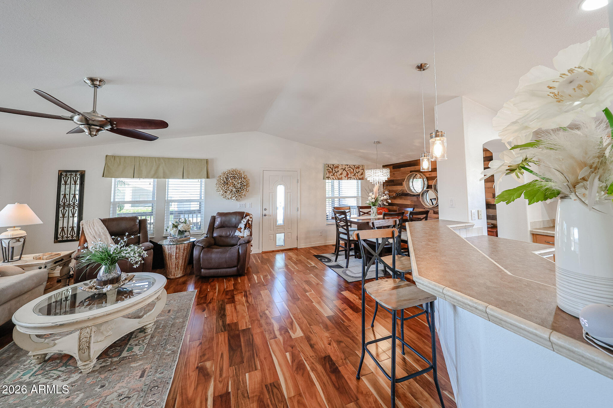 Open-plan living and dining room with leather recliners, a kitchen peninsula, and glossy hardwood floors.