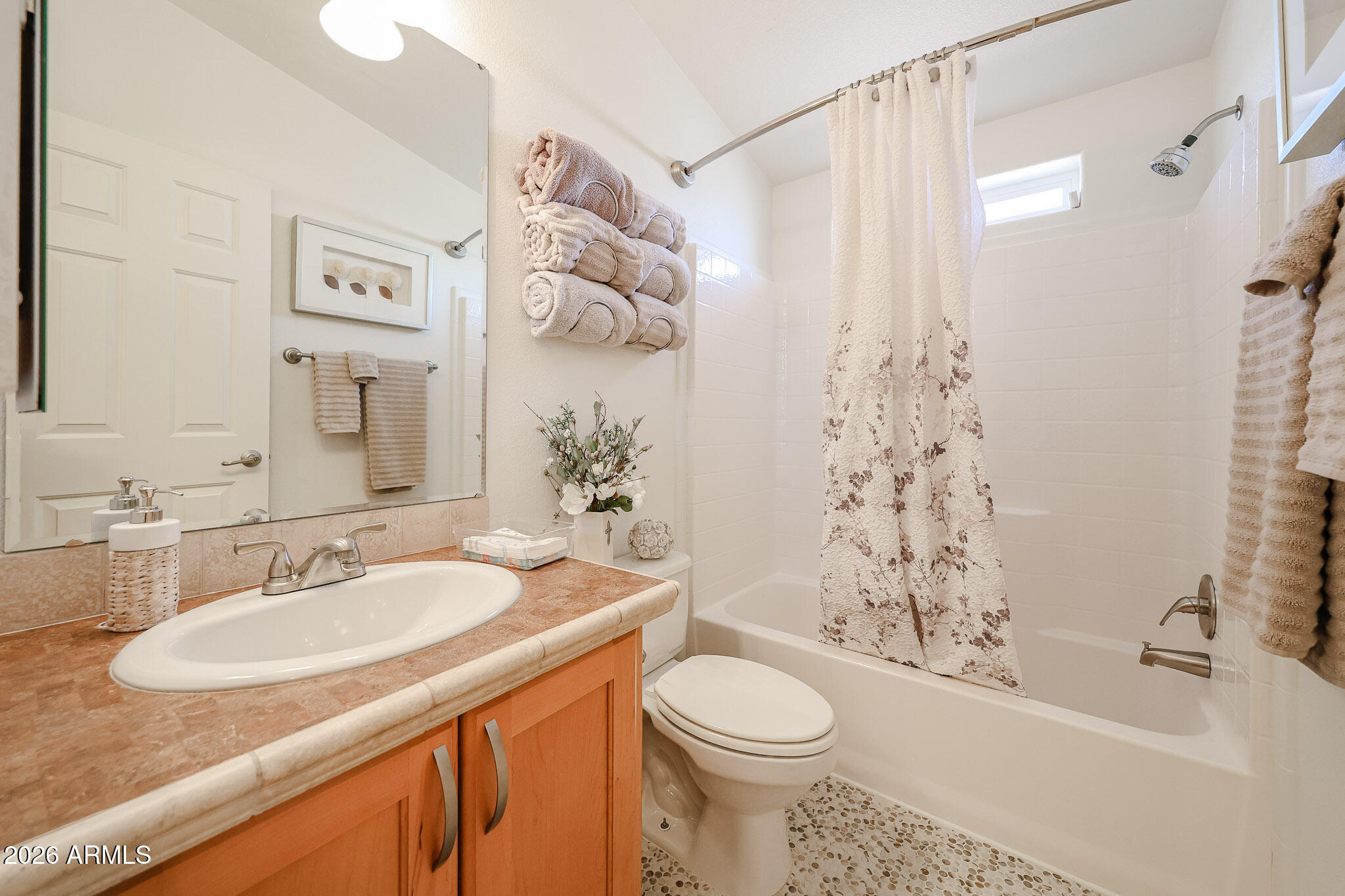 Bathroom with a peach-toned vanity, oval sink, and tub with a floral shower curtain.