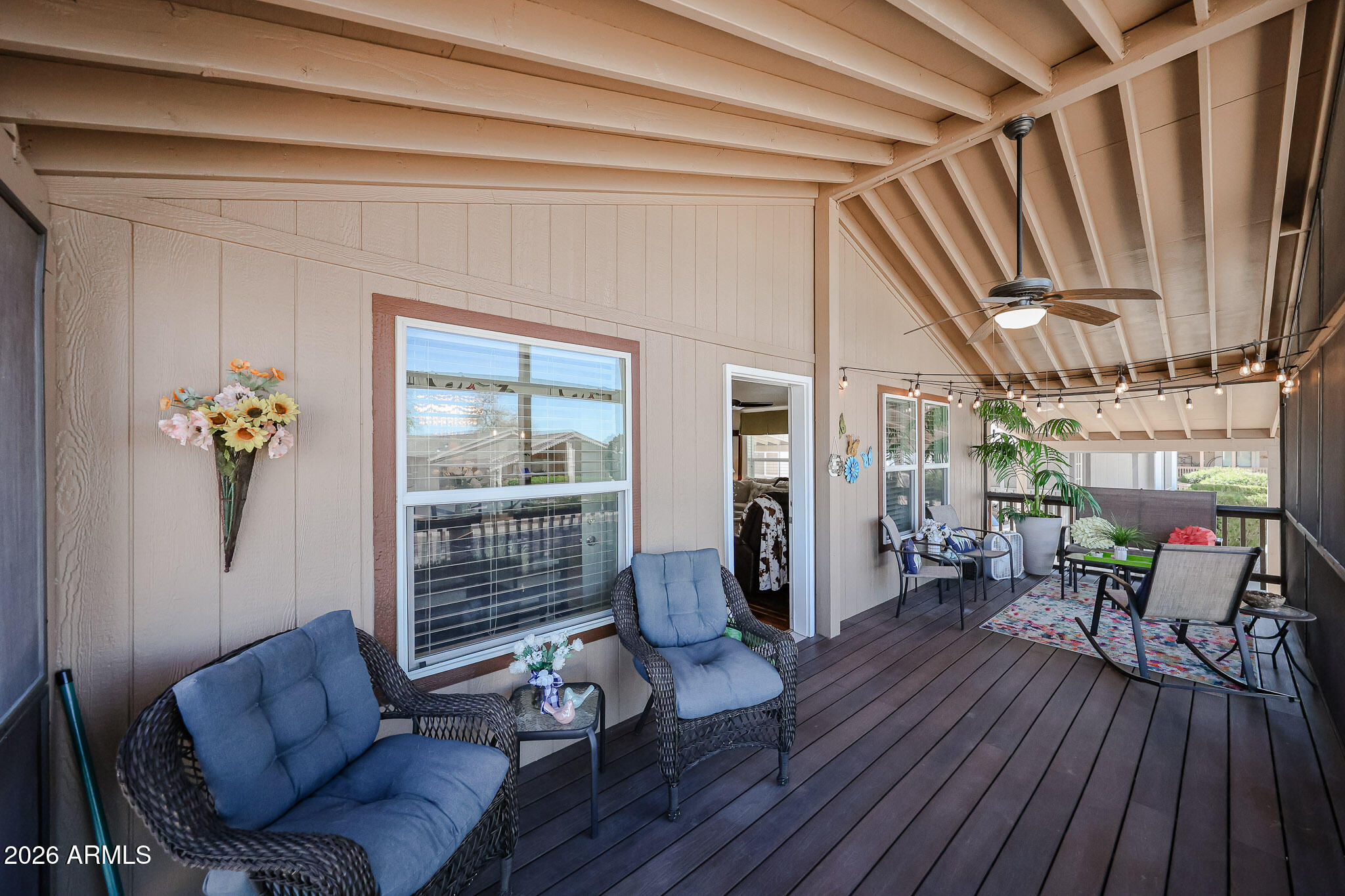 Covered patio with a vaulted beam ceiling, blue-cushioned wicker chairs, and string lights.