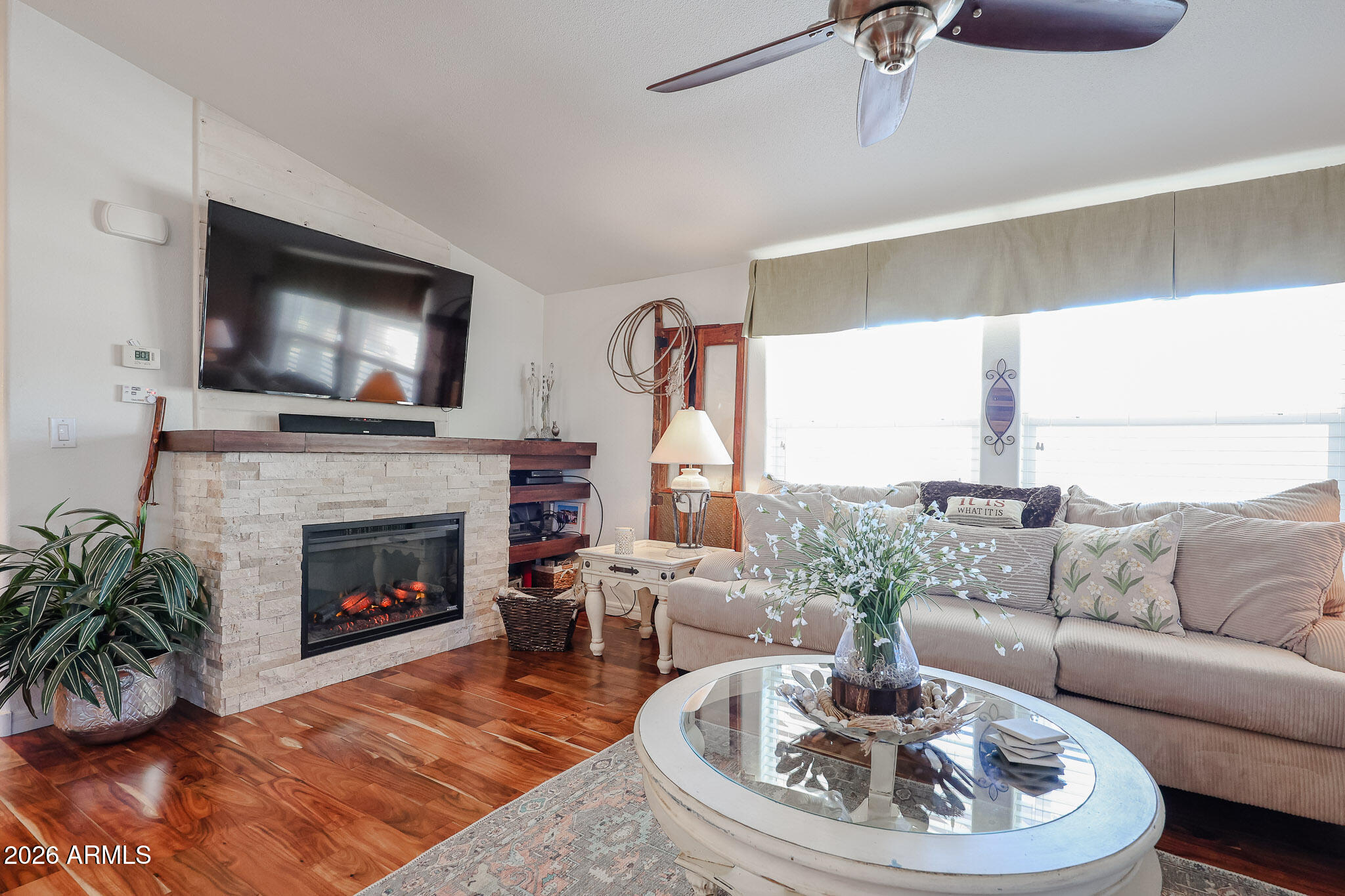 Living room with a stone fireplace, mounted television, beige sofa, and oval glass coffee table.