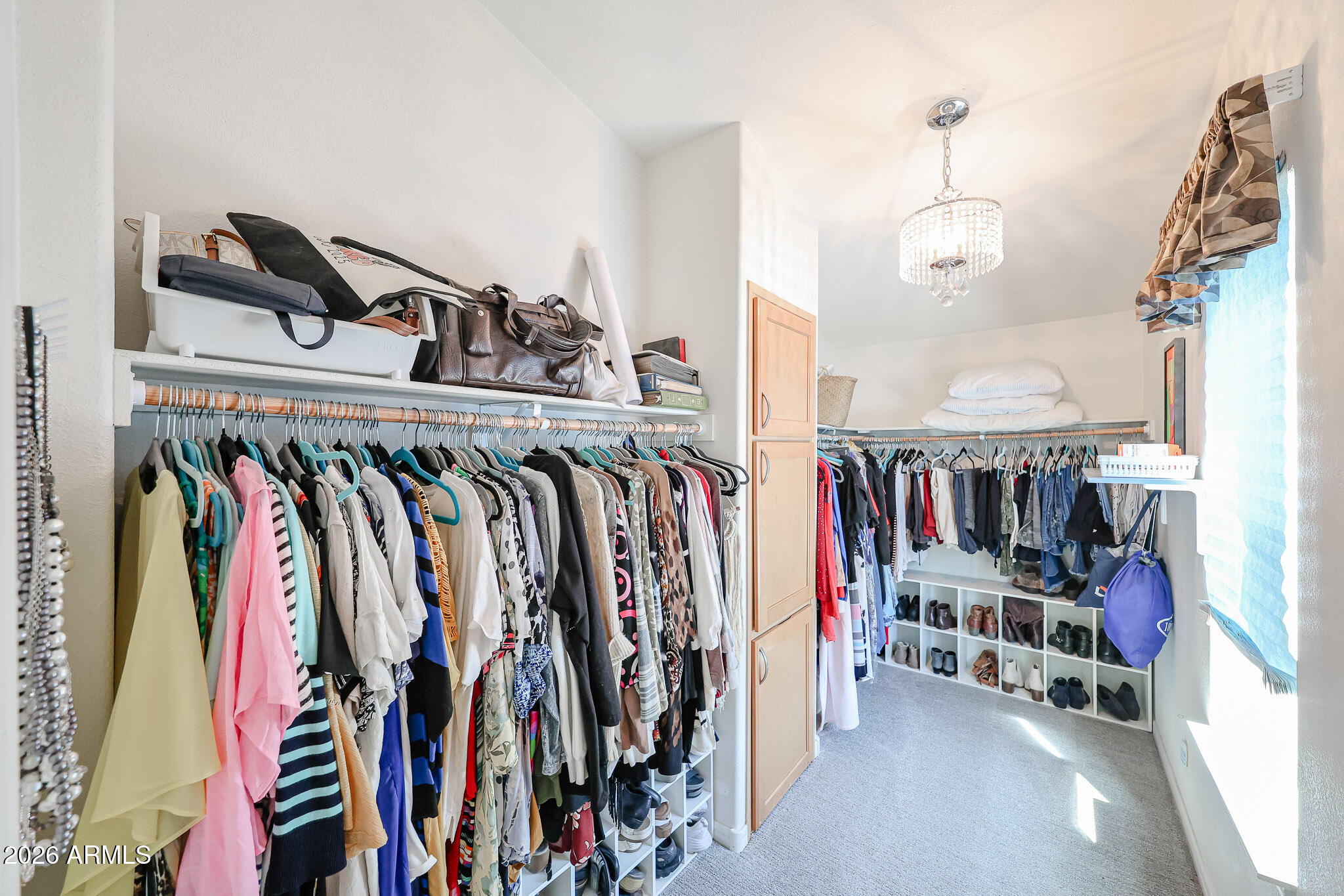 Walk-in closet with extensive clothing racks, shoe cubbies, and a chandelier.