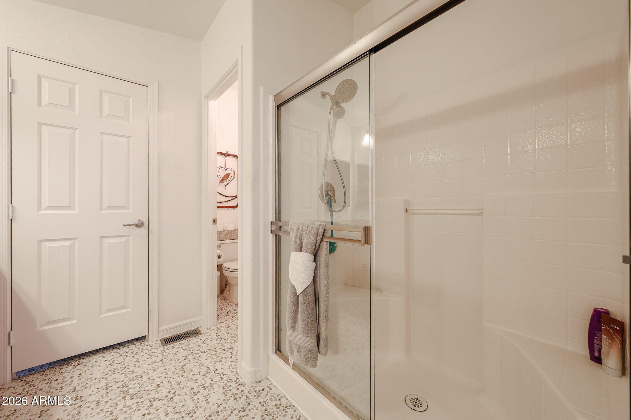 Bathroom with a glass-enclosed tiled shower and pebble-pattern floor.