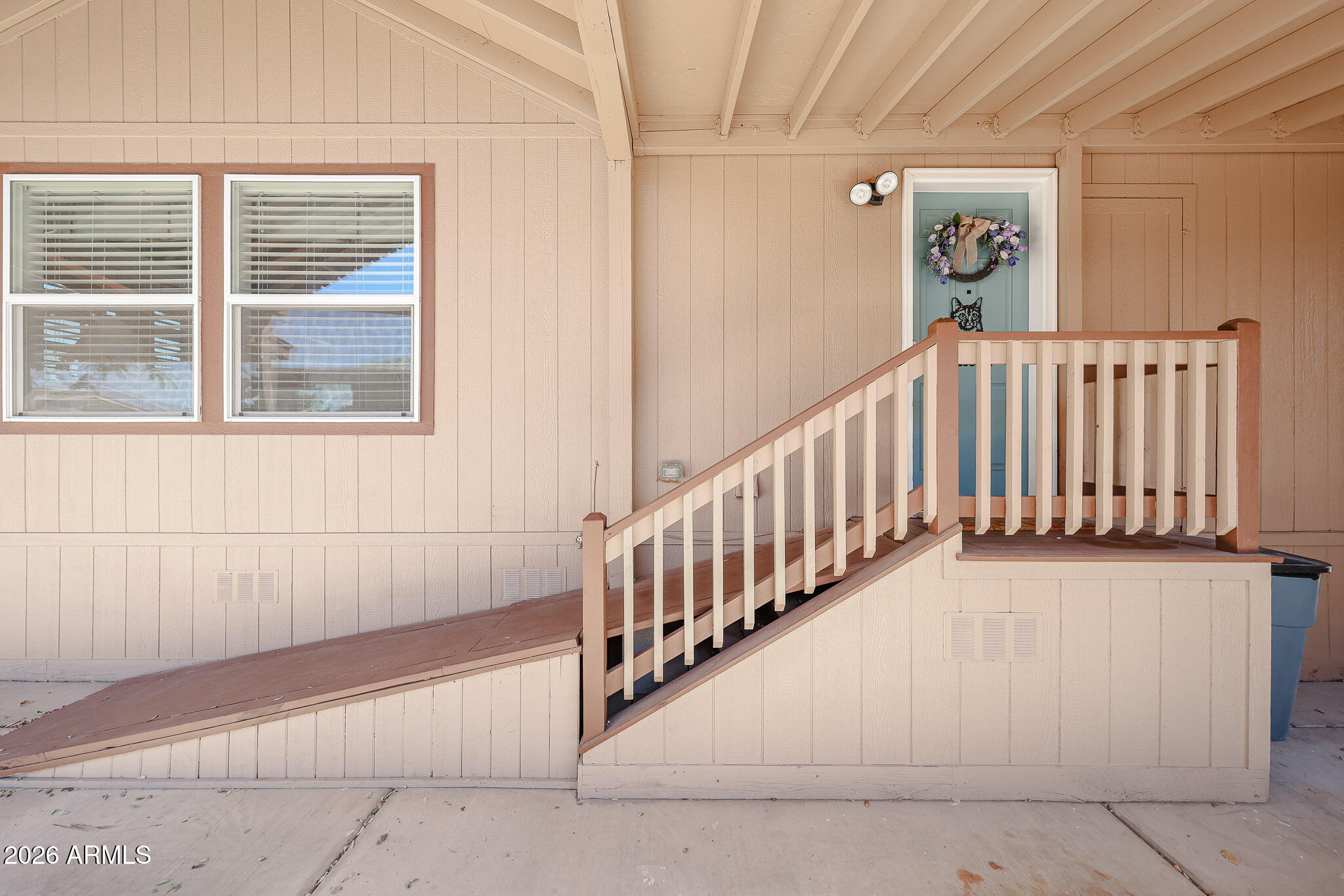 Covered home entrance with a long ramp, railing, two windows, and a blue door with a wreath.