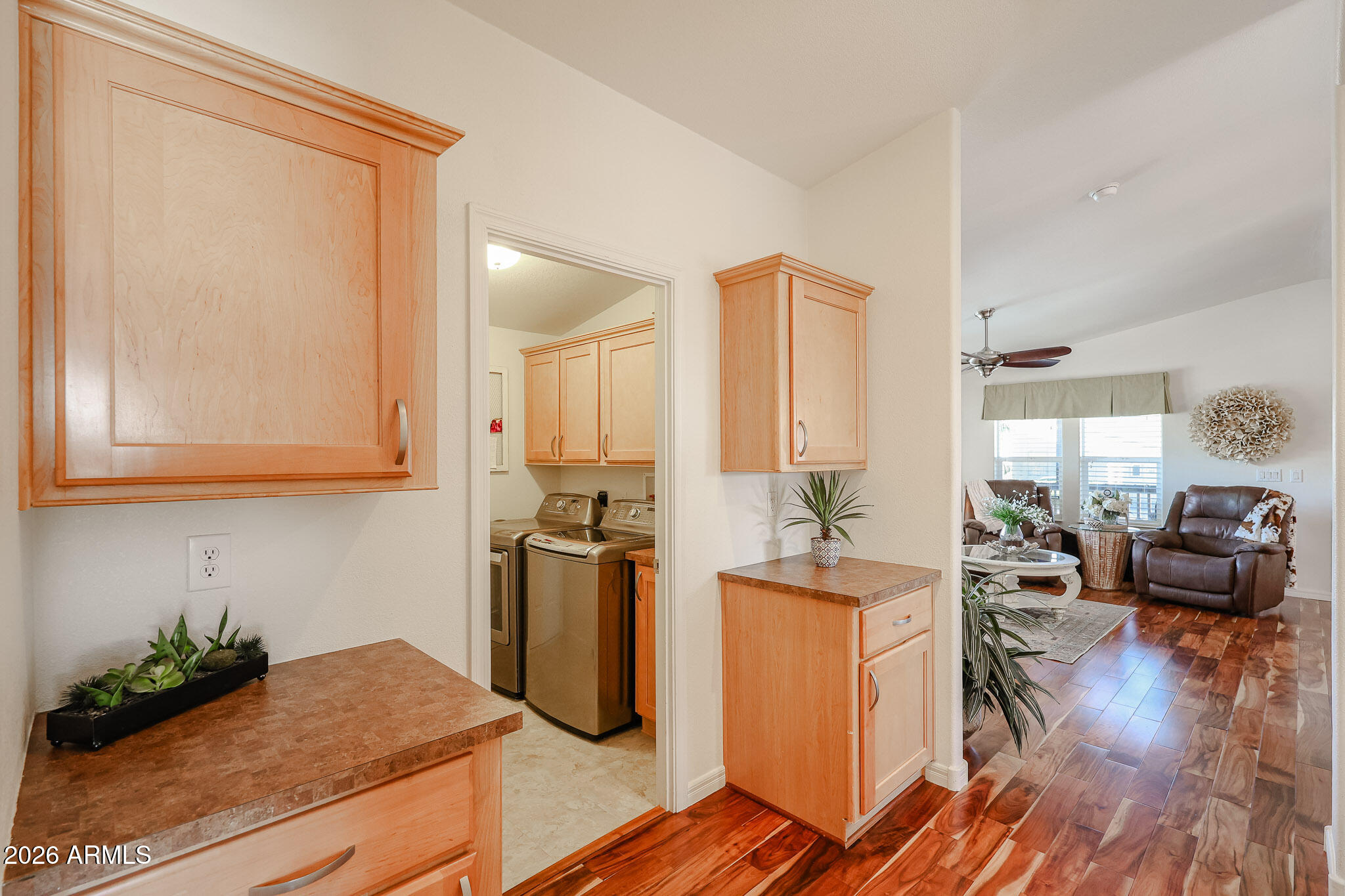 Laundry area with washer and dryer, light wood cabinetry, and a view into the furnished living room.