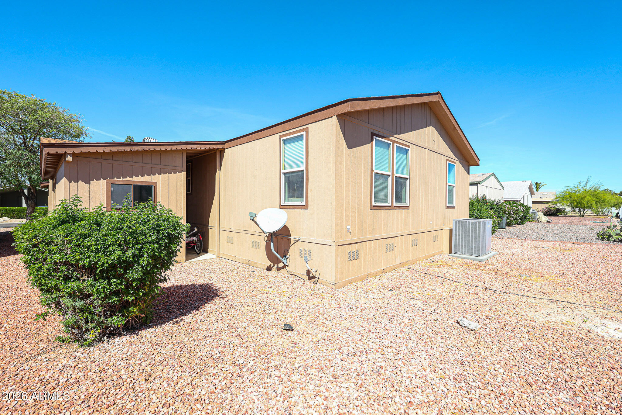 Tan single-story home with brown trim, gravel landscaping, and a satellite dish.