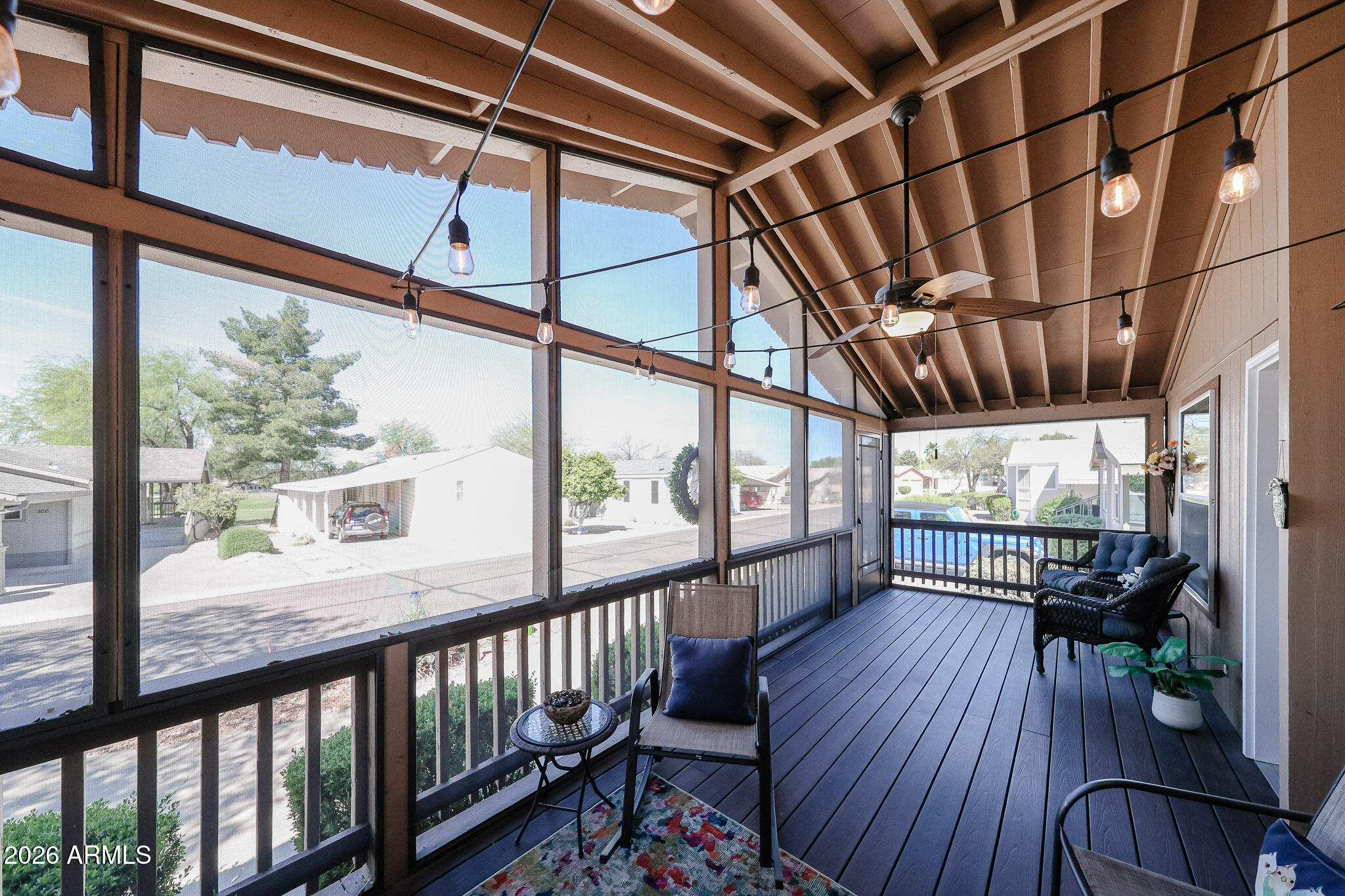Screened-in porch with vaulted wood beams, string lights, and seating overlooking the neighborhood.