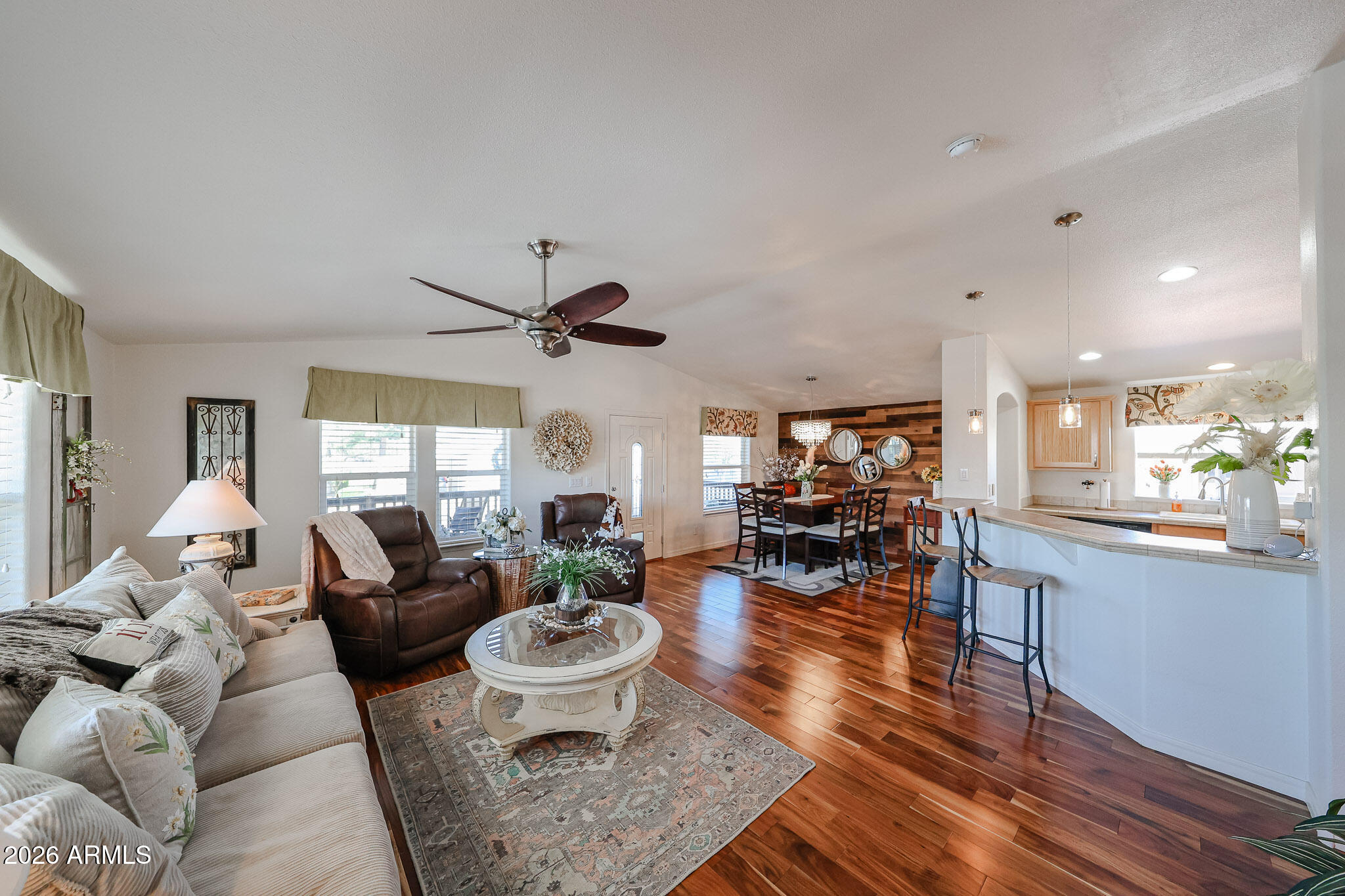 Open-plan living room and kitchen with reddish wood floors, a breakfast bar, and a dining area.