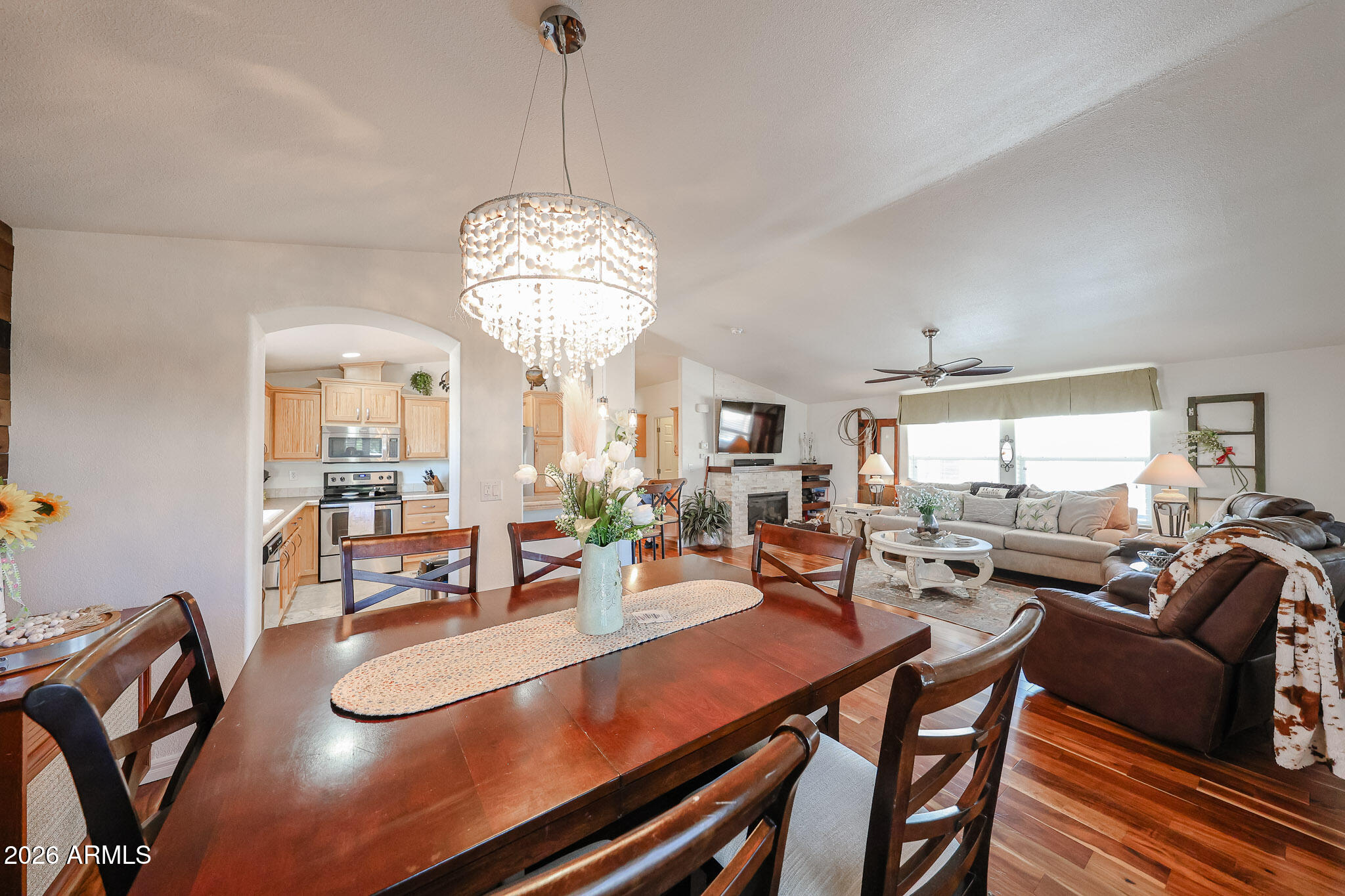 Open-plan dining and living area with a crystal chandelier, dark wood table, fireplace, and light wood kitchen cabinets.