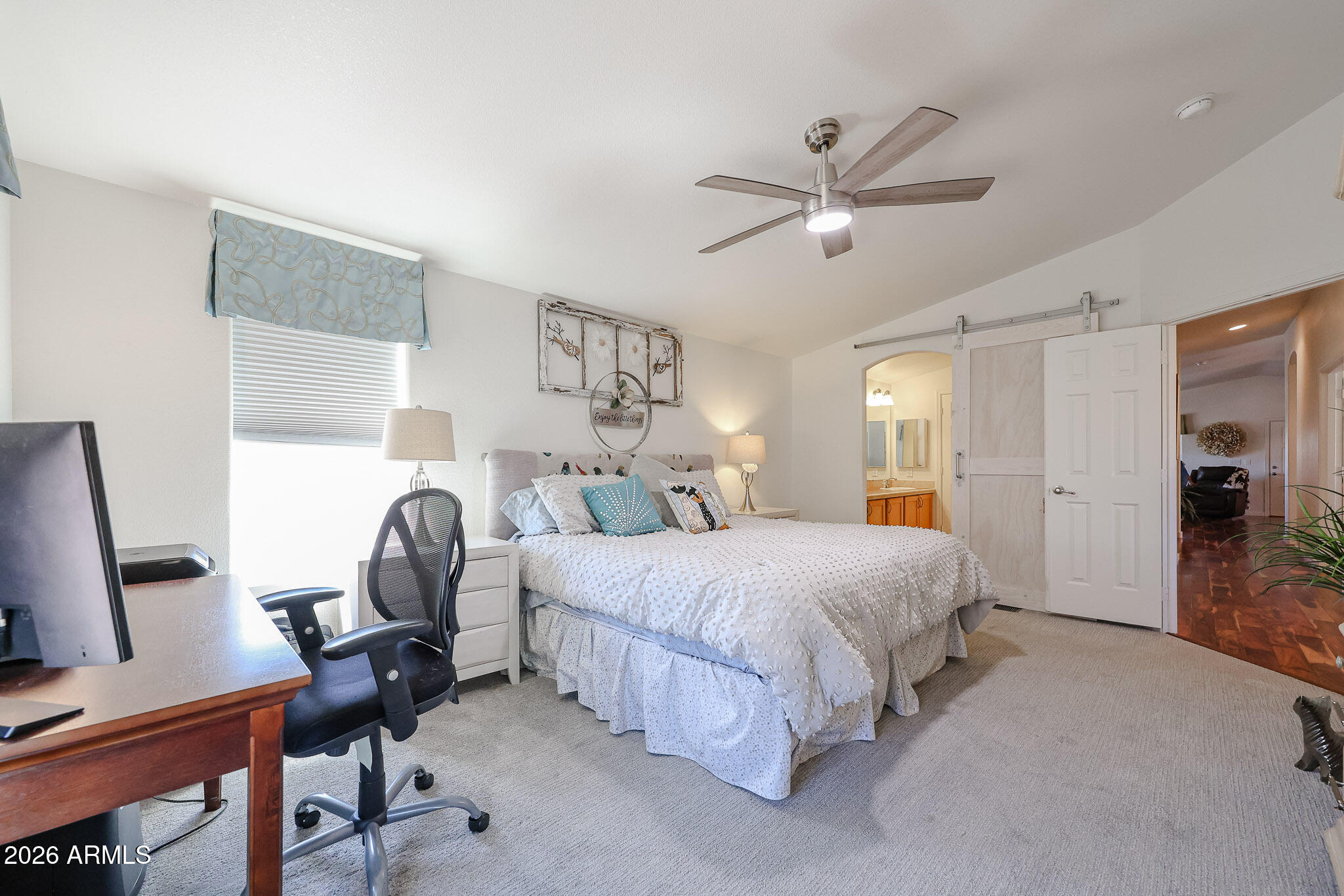 Bedroom with a large white bed, ceiling fan, and desk beside the window.