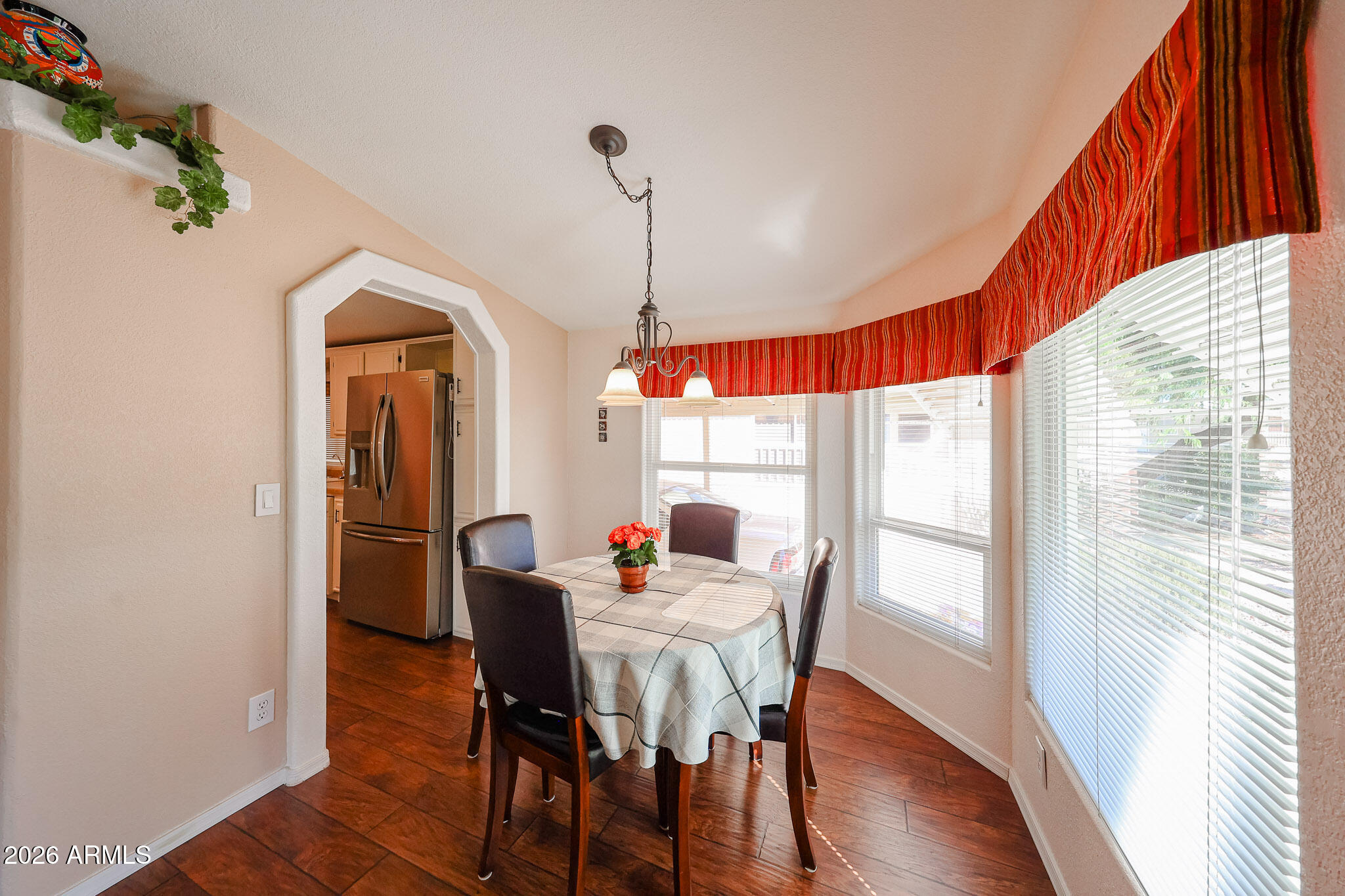 Dining area with a round table beside bright windows and an arched kitchen doorway.