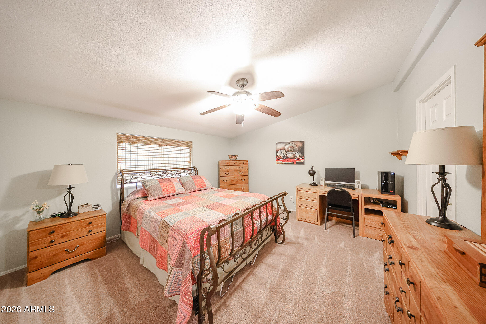 Bedroom with a metal bed, colorful patchwork quilt, wooden furniture, and a desk with a computer.