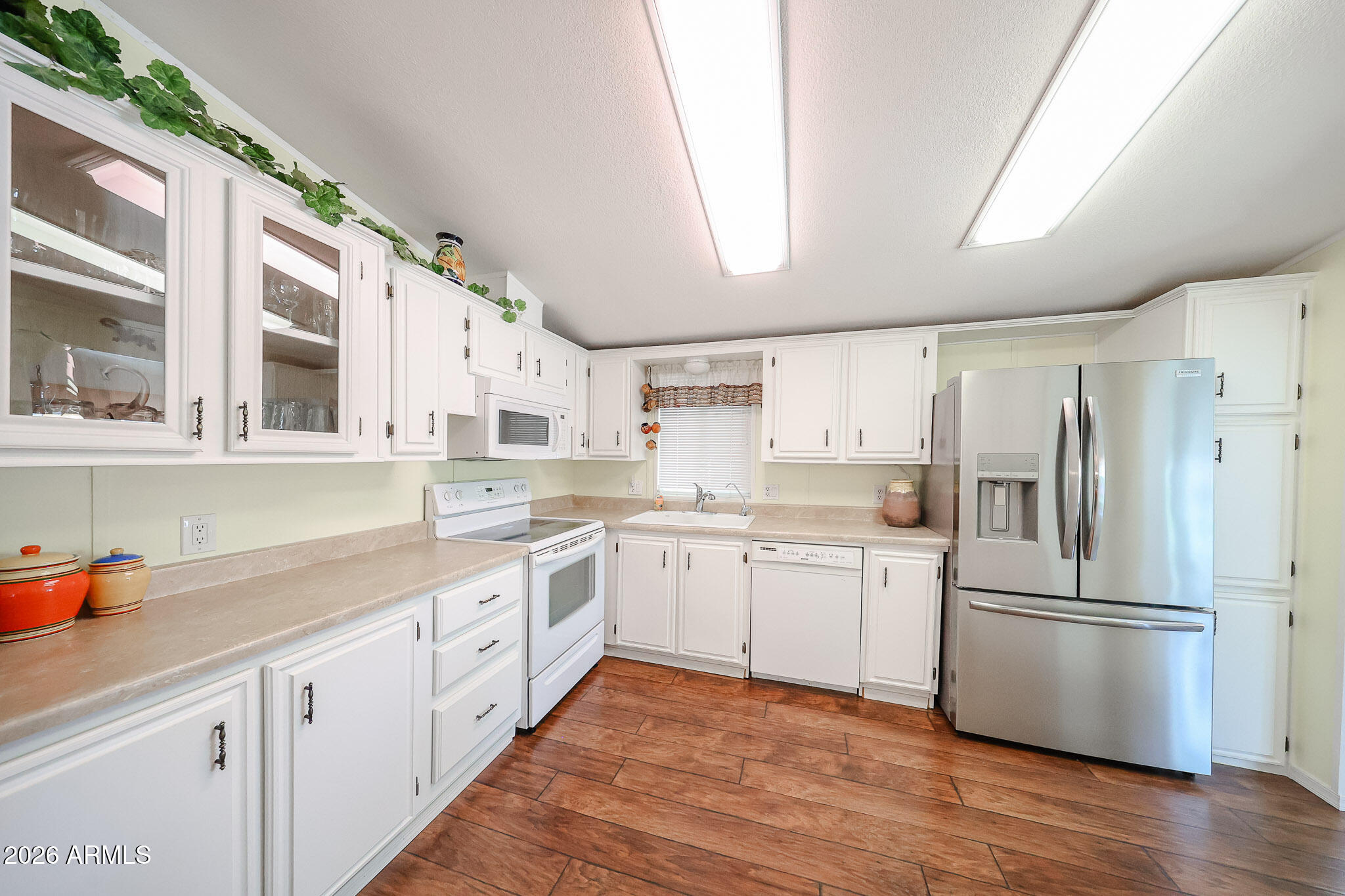 Kitchen with white cabinetry, stainless steel refrigerator, and warm wood-look tile flooring.