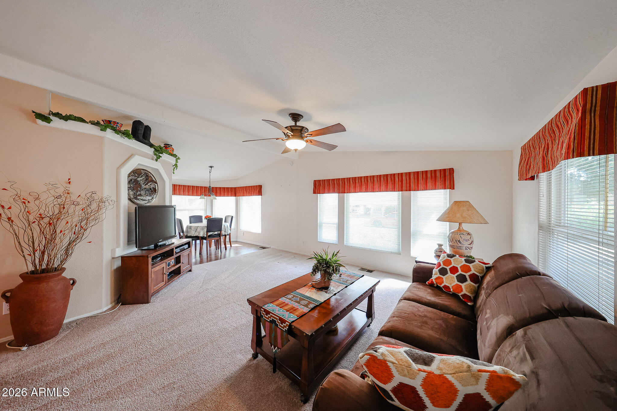Furnished living room with brown sofas, a wooden coffee table, and bright windows with blinds.