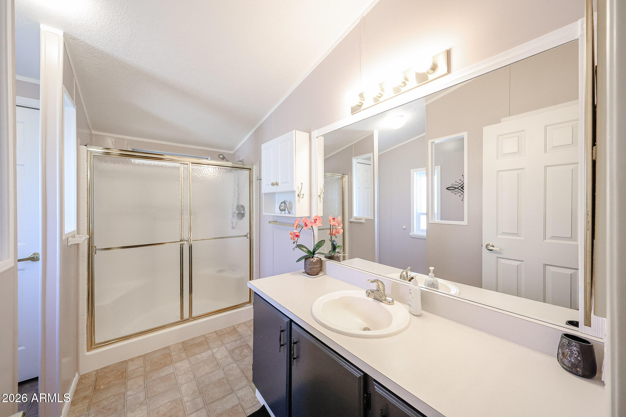 Bathroom with mirrored vanity and frosted-glass shower enclosure with gold-tone framing.