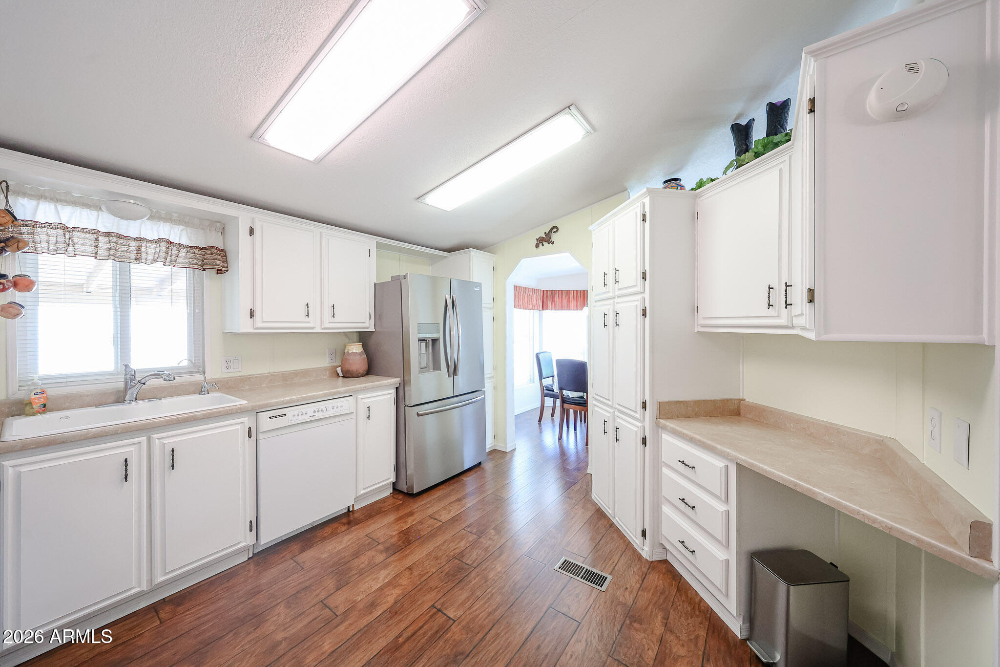 Bright kitchen with white cabinetry, stainless-steel refrigerator, beige counters, and wood-look flooring.