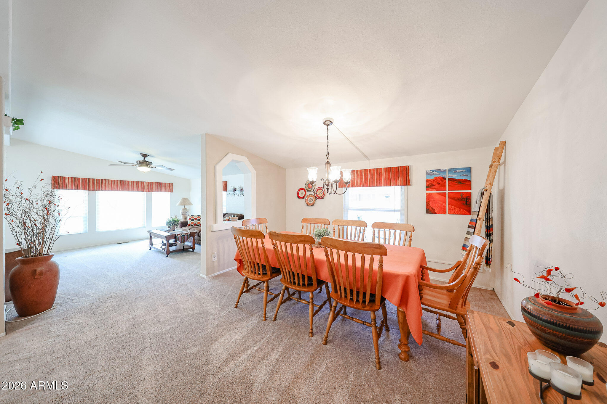 Dining room with a wooden table and chairs, coral tablecloth, chandelier, and adjoining bright living area.