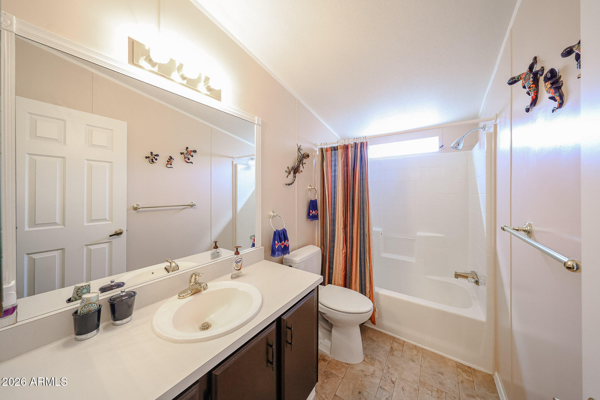 Bathroom with a long mirrored vanity and white tub-shower behind a striped curtain.