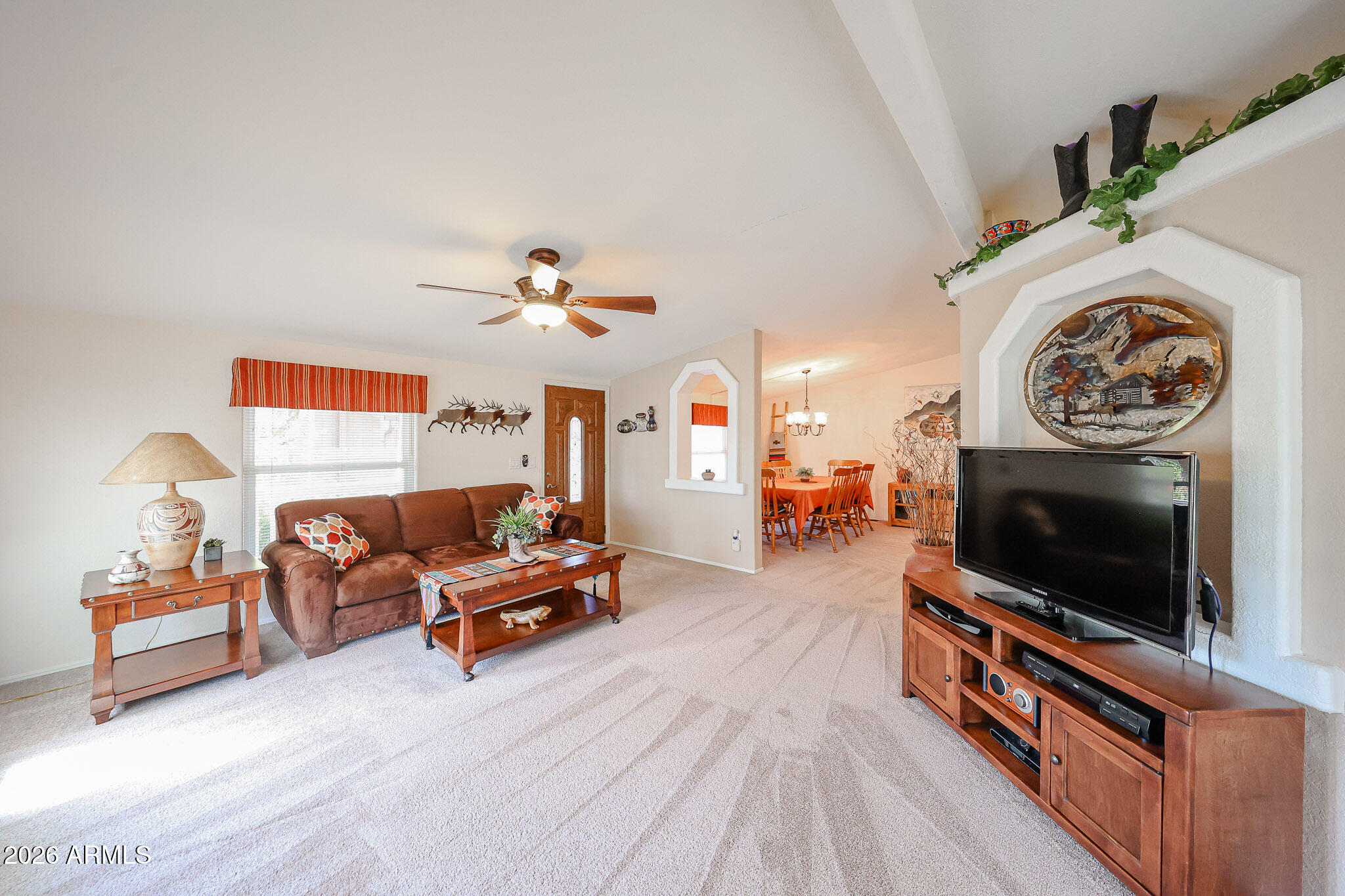 Furnished living room with brown sofa and television beside an arched opening to the dining area.