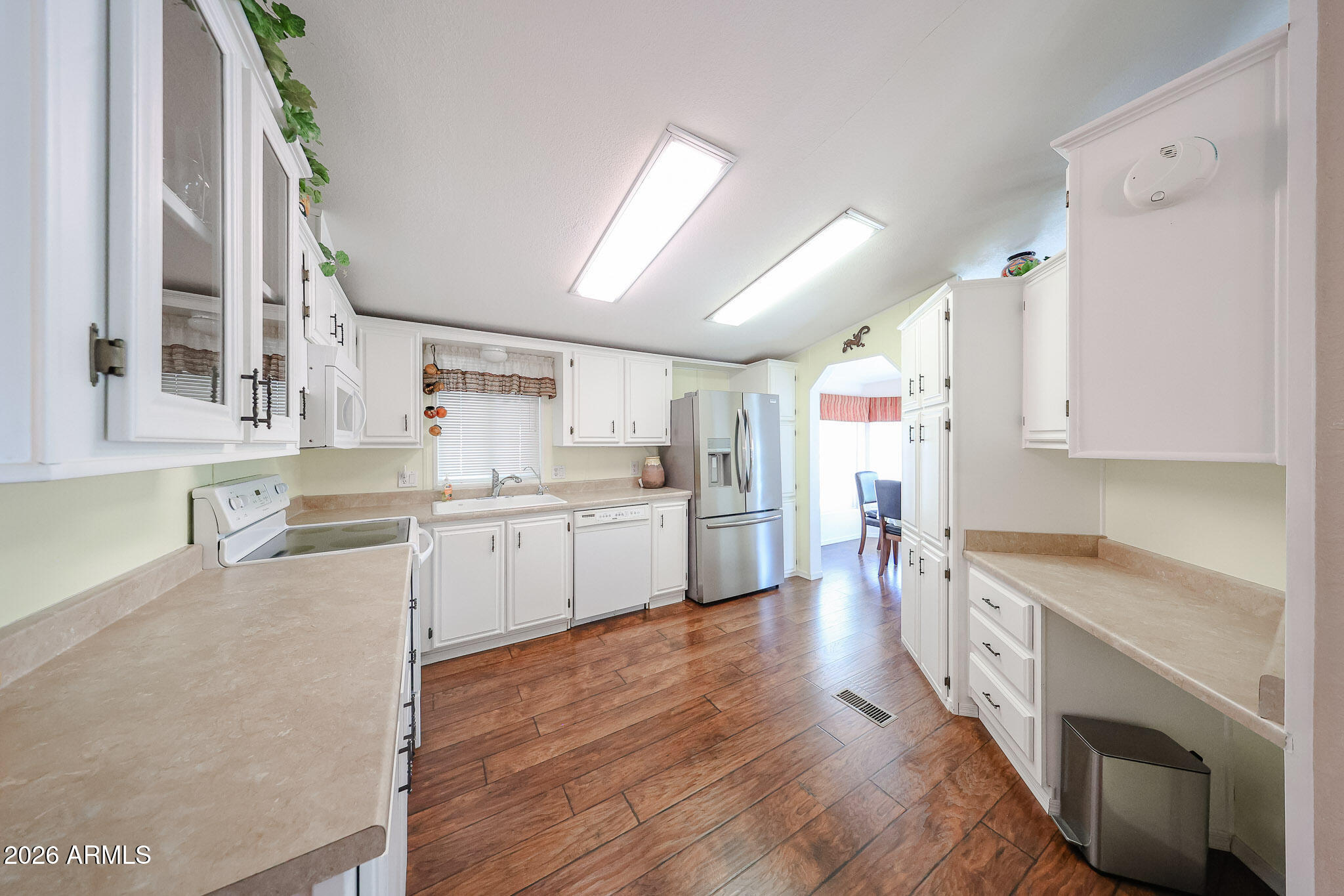 Kitchen with white cabinetry, beige counters, stainless refrigerator, and wood-look tile floors.